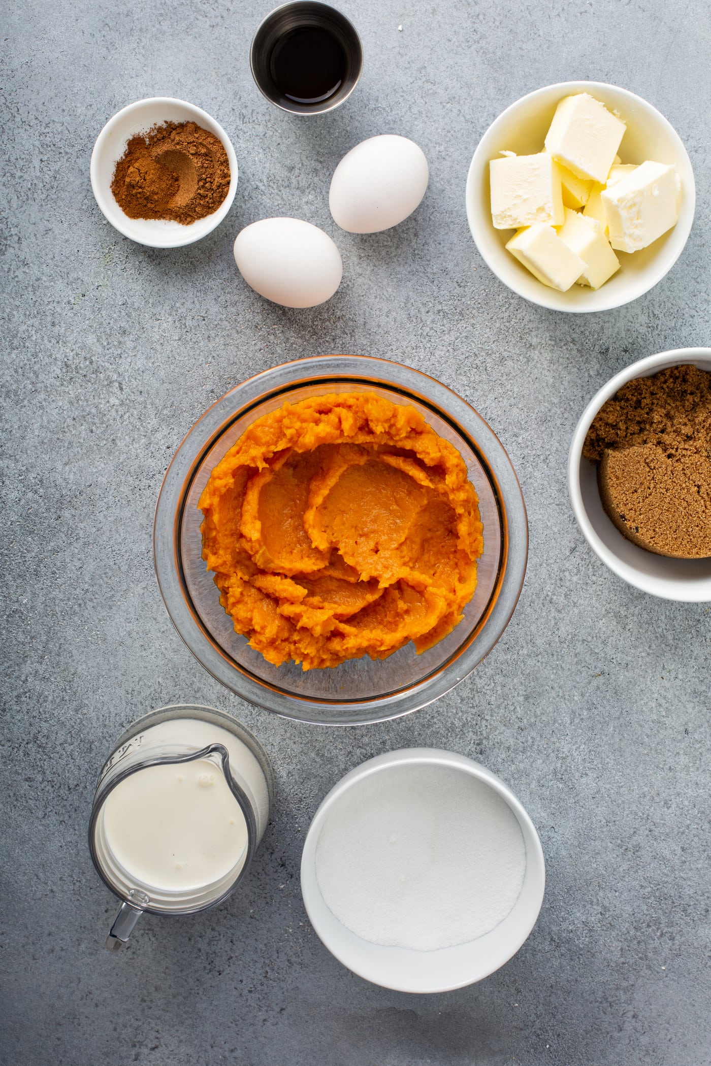 A photo of all the ingredients for sweet potato pie in separate bowls - pureed sweet potatoes, dark brown sugar, butter, two eggs, vanilla, sugar, cream, and cinnamon.
