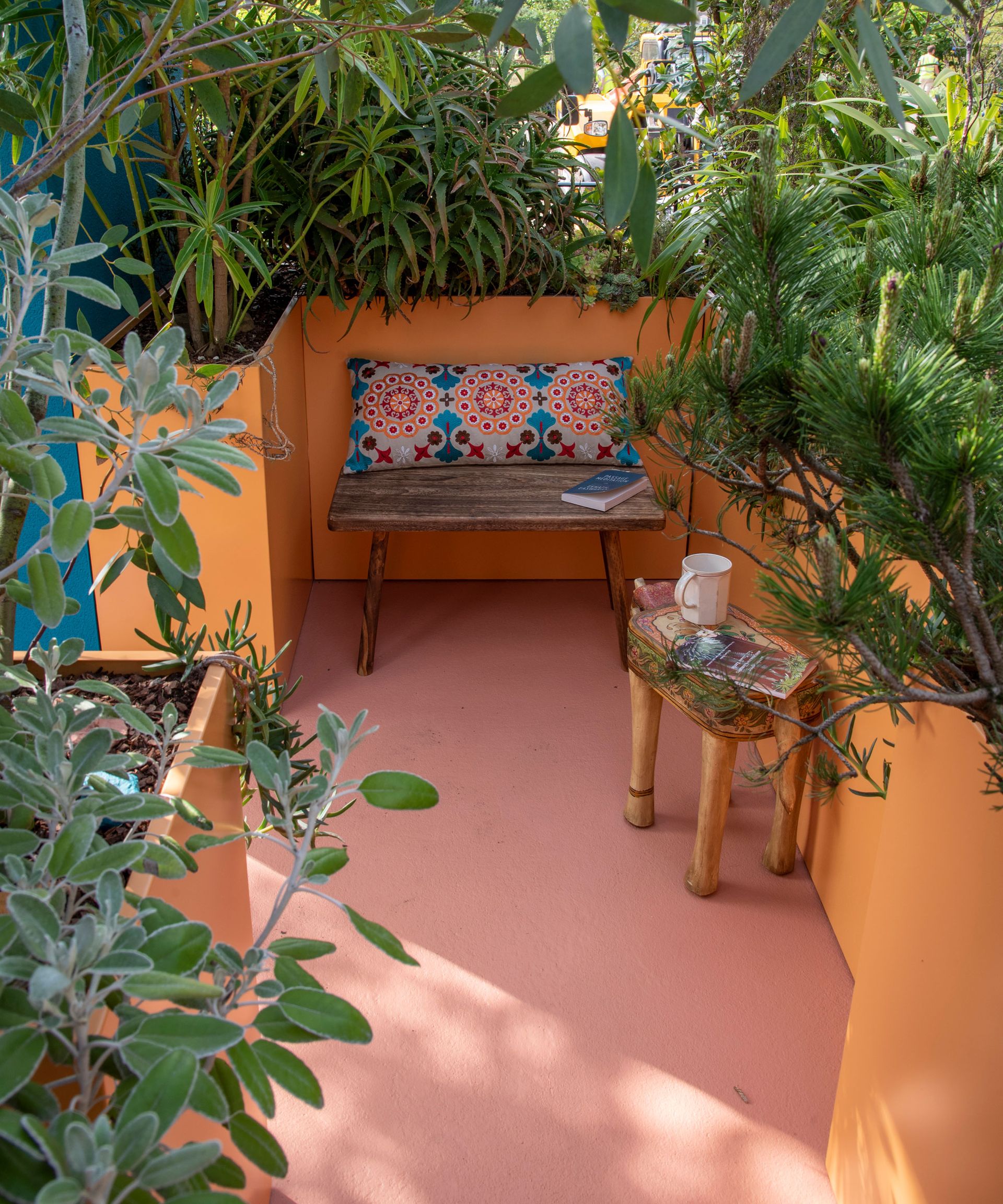 small patio garden with raised beds painted orange and filled with tropical plants, with a small bench and table