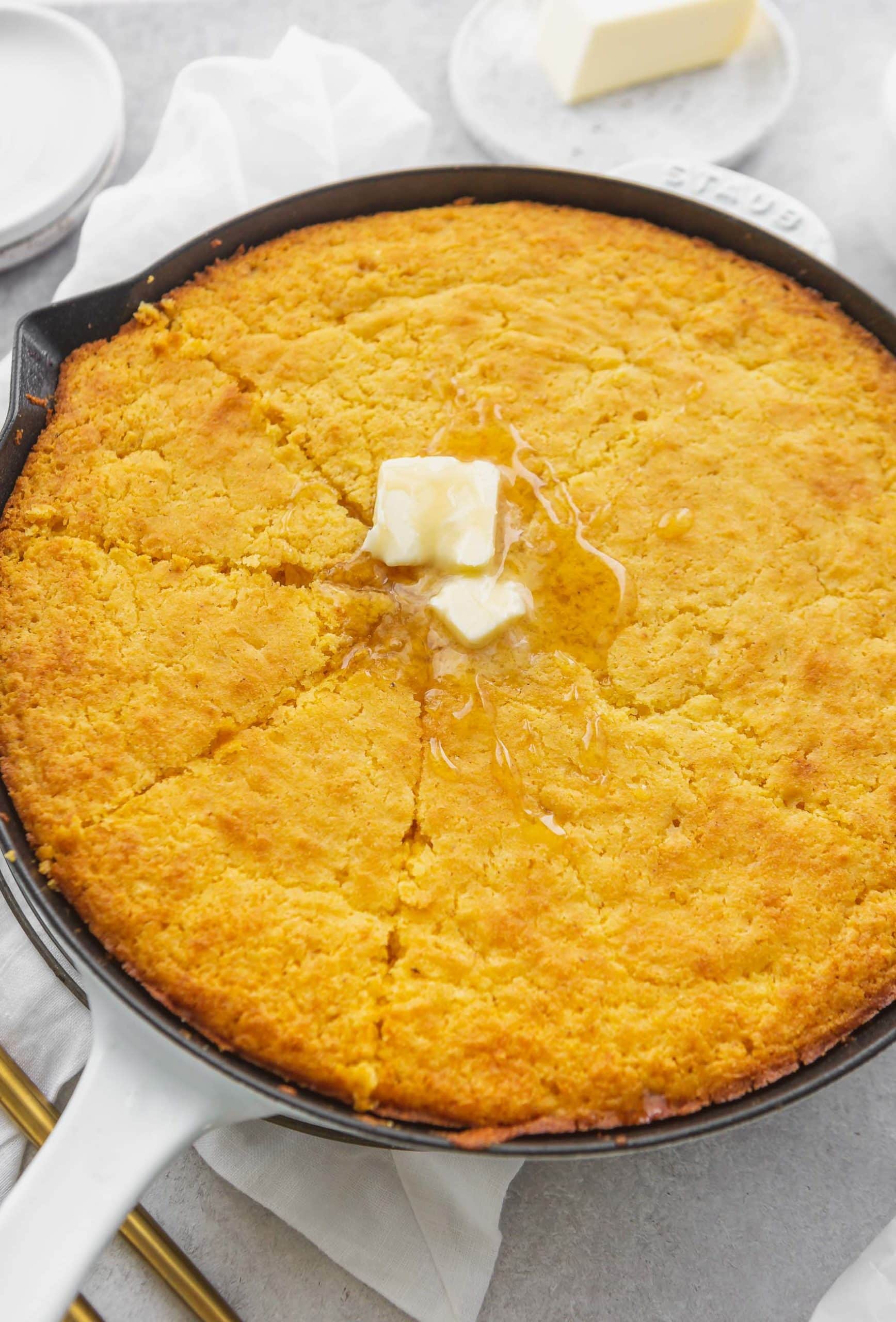 A cast iron skillet with baked cornbread. The cornbread has been sliced and there are two melting patties of butter on top.
