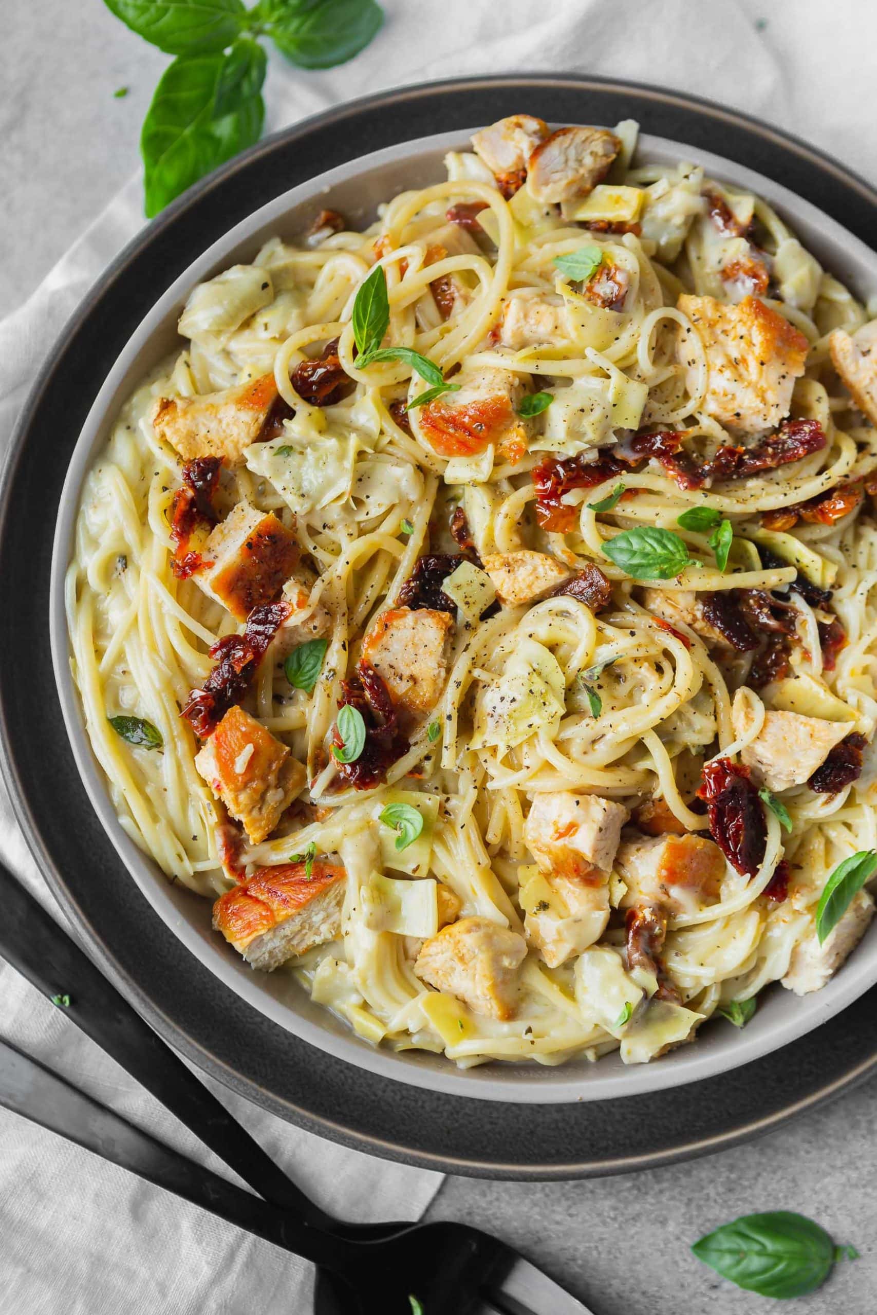 a photo of creamy chicken pasta topped with sun dried tomatoes, golden chicken chunks and fresh basil.