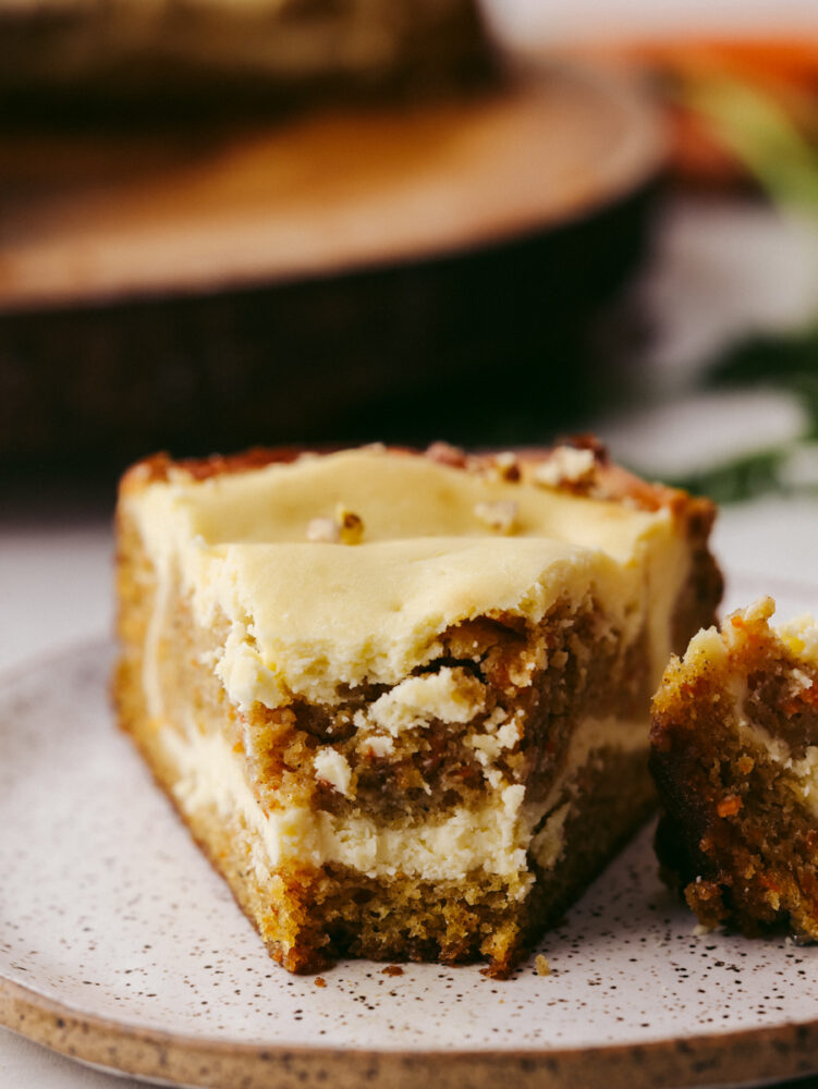 Closeup of a slice of carrot cake cheesecake with a bite taken out of it.