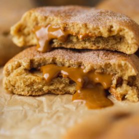 A biscoff stuffed snickerdoodle broken in half and the halves are stacked on top of each other. The biscoff center is oozing out onto the parchment paper.