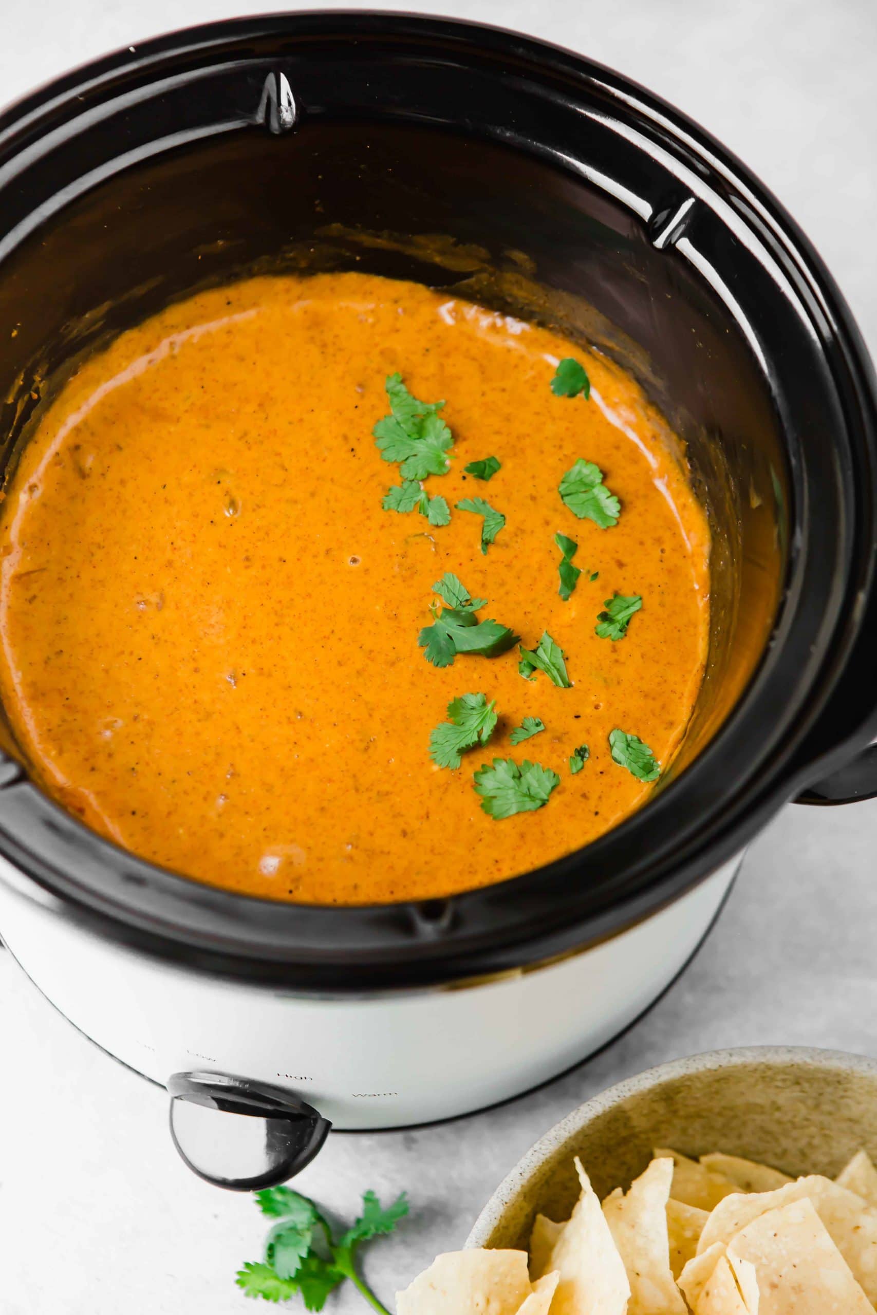 A slow cooker full of chilis queso dip. there are a few parsley leaves scattered on top.