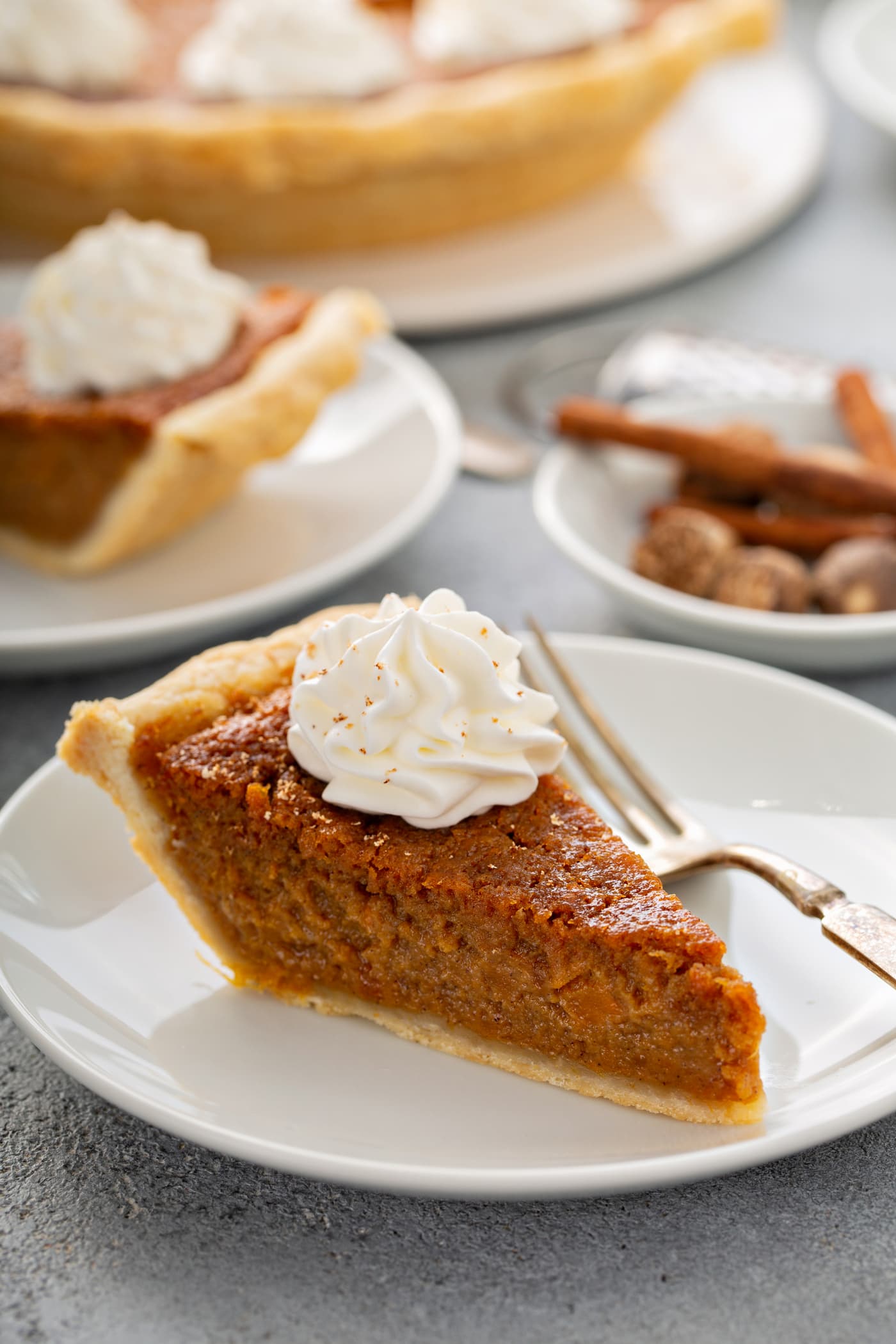A photo of a slice of sweet potato pie with a dollop of whipped cream on top sitting on a white plate.