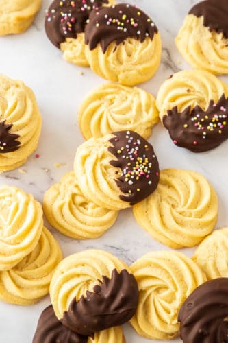 A batch of butter cookies, some chocolate coated, spread over a marble bench top