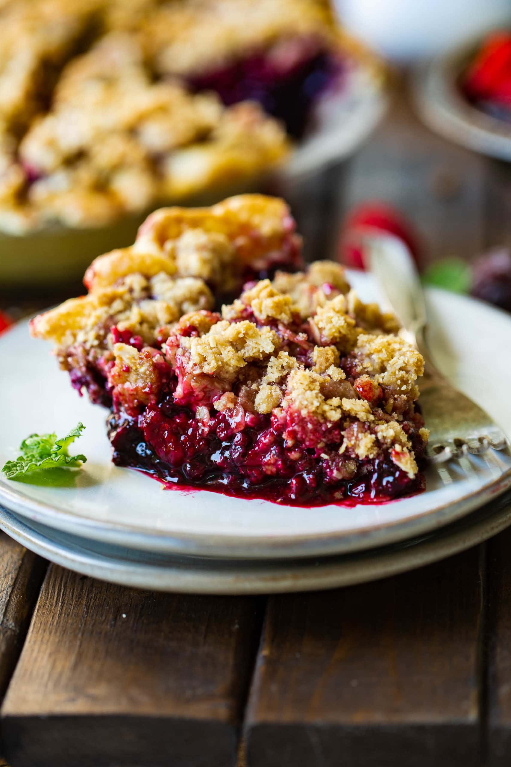 a photo of a piece of dutch berry pie sitting on a small white dessert plate with an oat streusel on top and golden crust on the bottom.