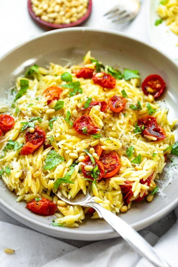 a photo of a large serving bowl full of cooked orzo pasta, roasted tomatoes and garlic and chopped fresh basil.