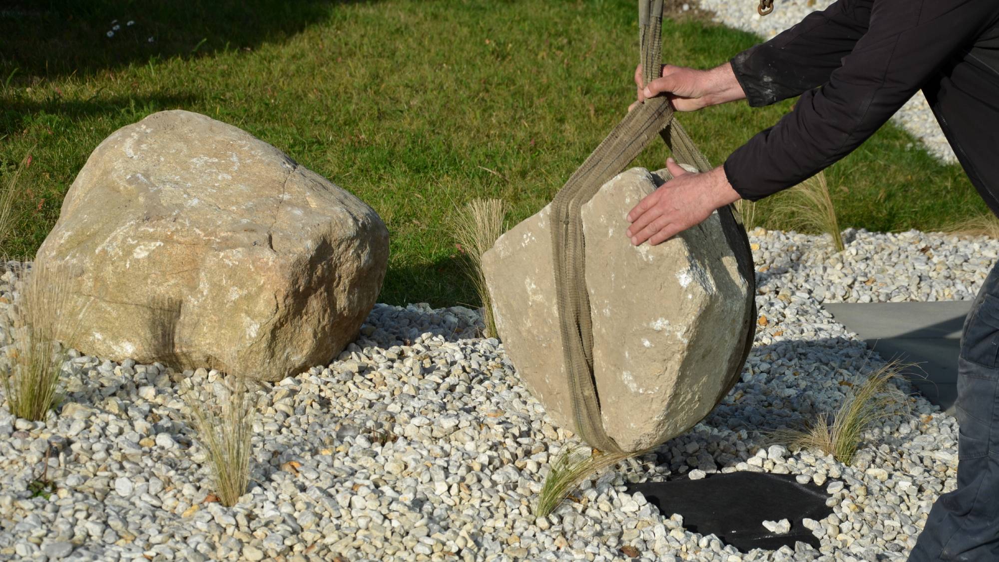 Hands guiding a large rock into a rock garden