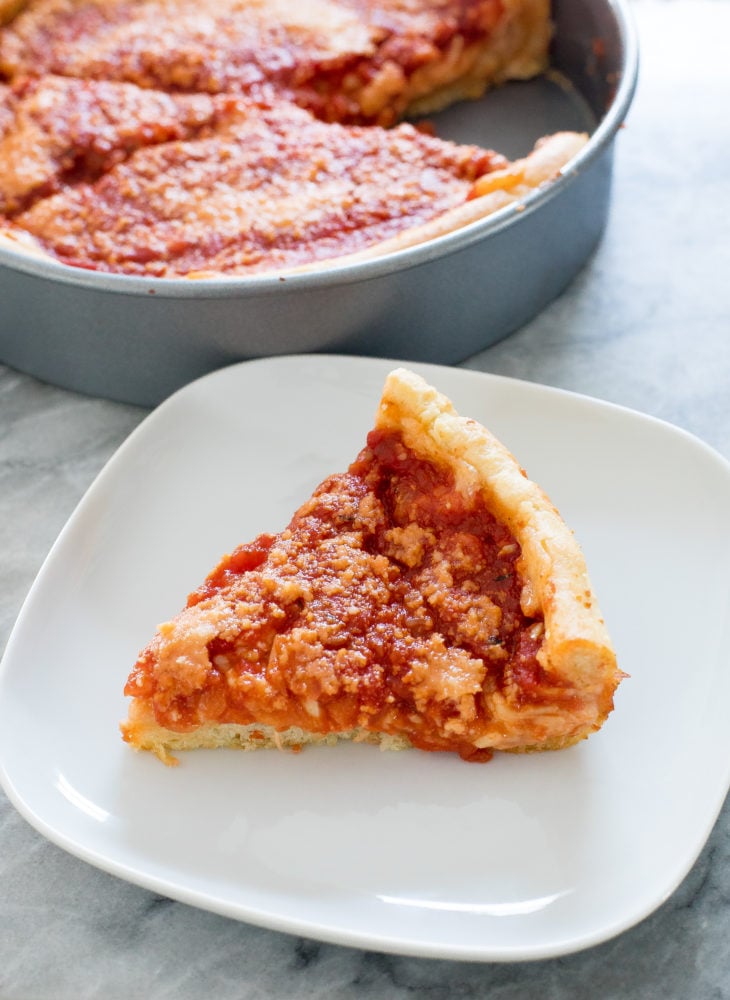 A slice of deep dish pizza sitting on a white plate.