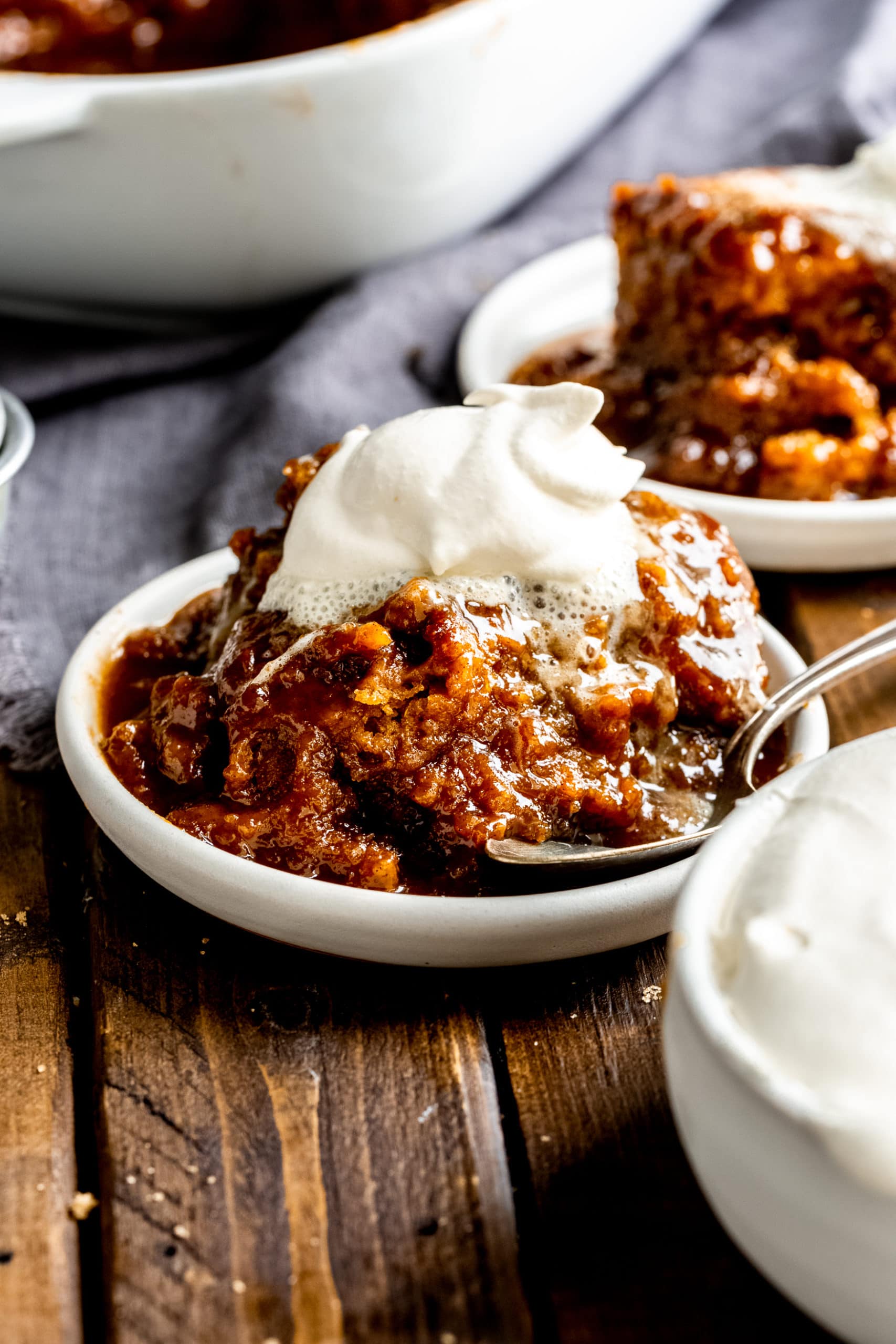 a photo of a single serving of pumpkin lava cake sitting on a small white saucer topped with a dollop of whipped cream. the cake is sitting in sauce that has seeped out of the cake.