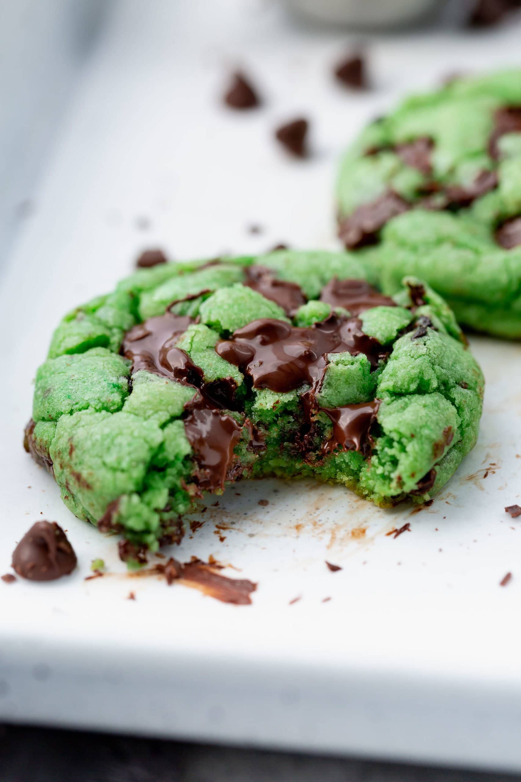 a close up of a green mint chocolate chip cookie with a bite taken out of it.