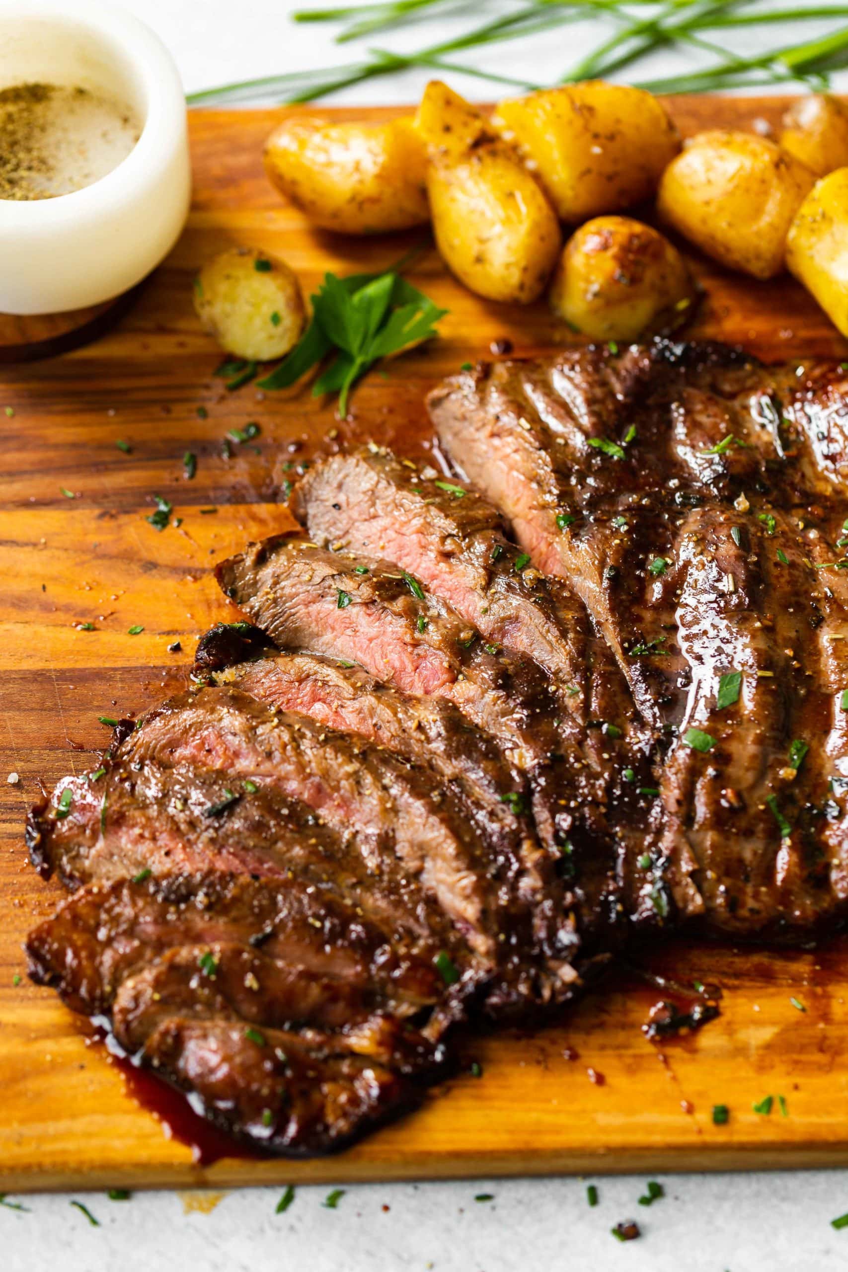 a cutting board with roasted yukon gold potatoes and sliced grilled flank steak with a delicious marinade