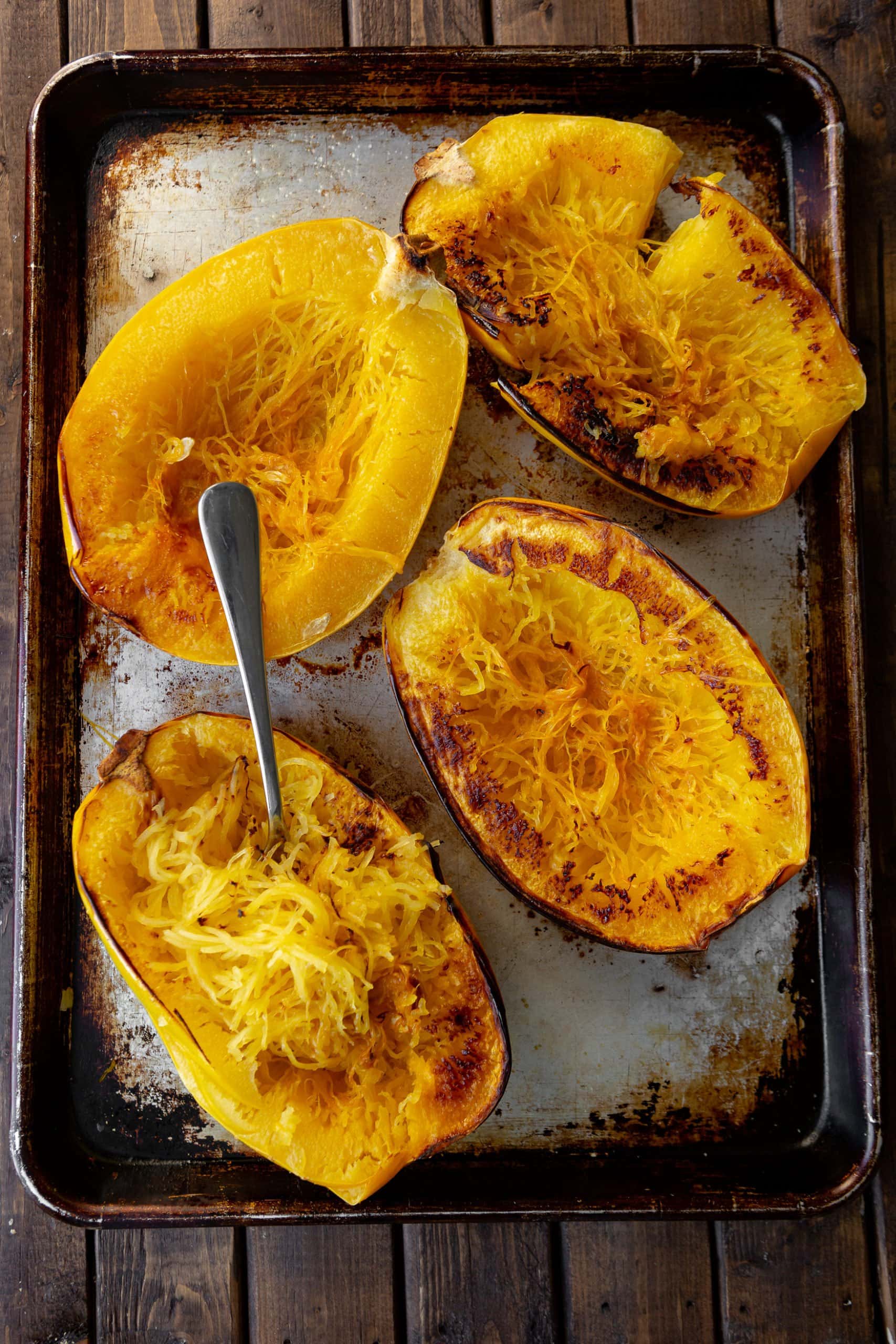 a photo of spaghetti squashes that have been sliced in half and roasted sitting on a baking sheet. They are golden brown and one of the halves has a fork sticking into it.