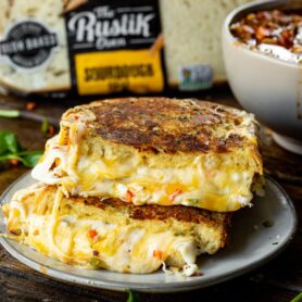 a photo of a golden grilled cheese sandwich that has been cut in half and stacked on top of each other with the facing the camera and gooey cheese melting out all the sides.