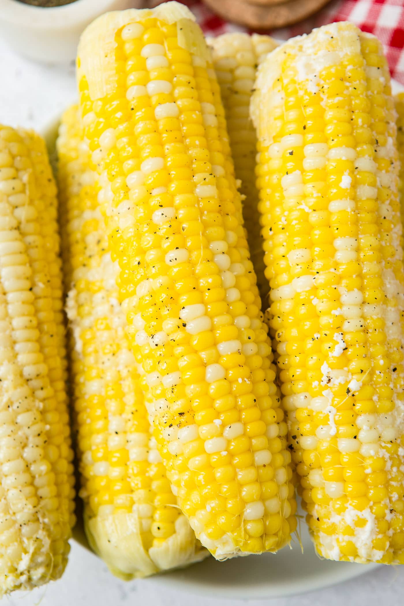 Four ears of cooked corn on the cob that has been lightly sprinkled with ground pepper.