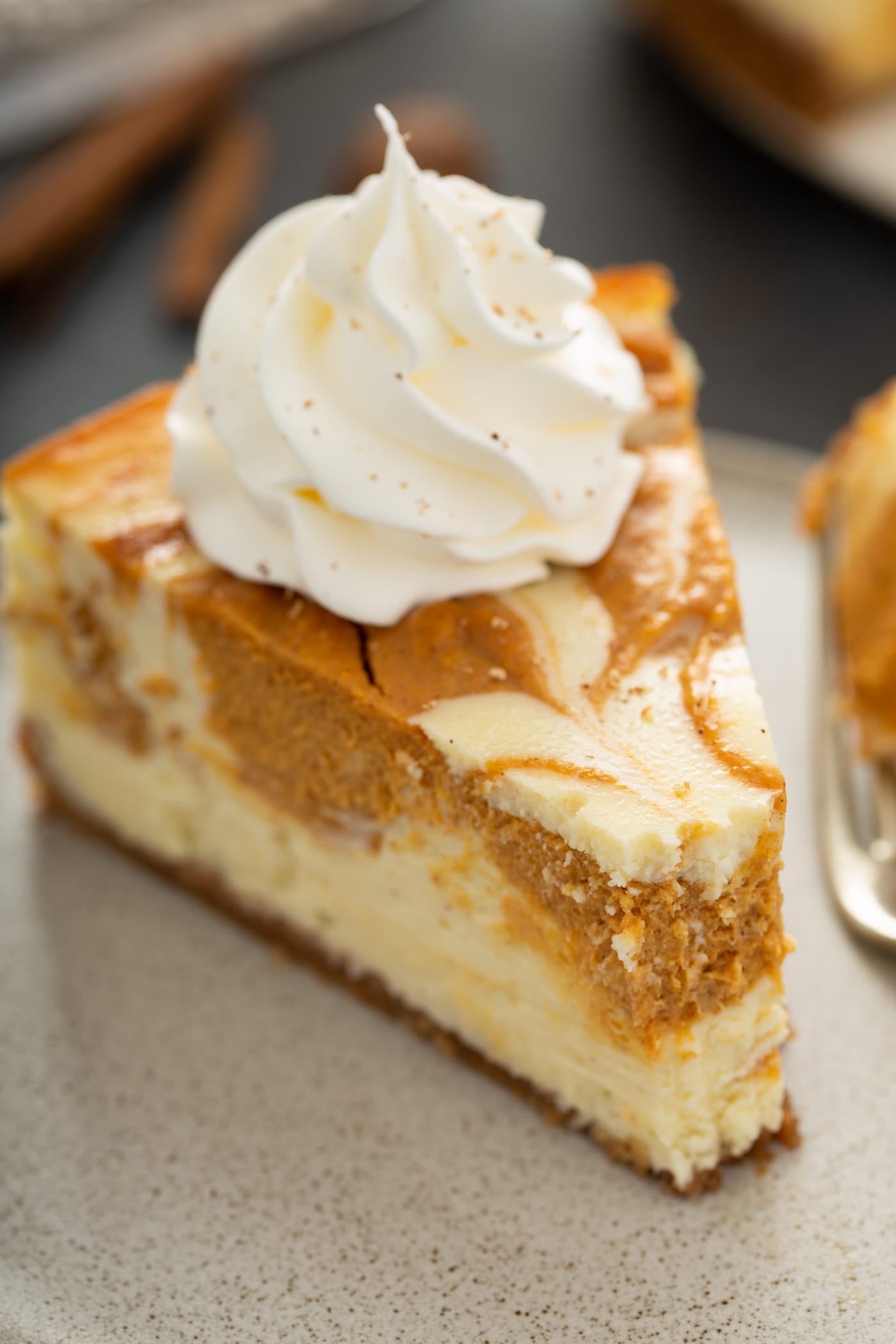A piece of swirled pumpkin cheesecake on a plate. It is topped with a dollop of whipped cream and a bite has been taken from the point of the slice.