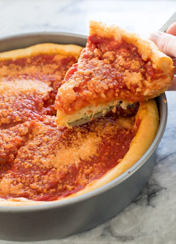 Deep dish pizza in a pan with a slice getting taken out. 
