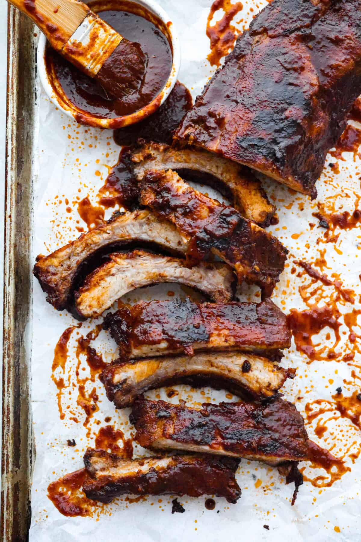 Slab of grilled BBQ ribs with a small bowl of sauce and a basting brush.