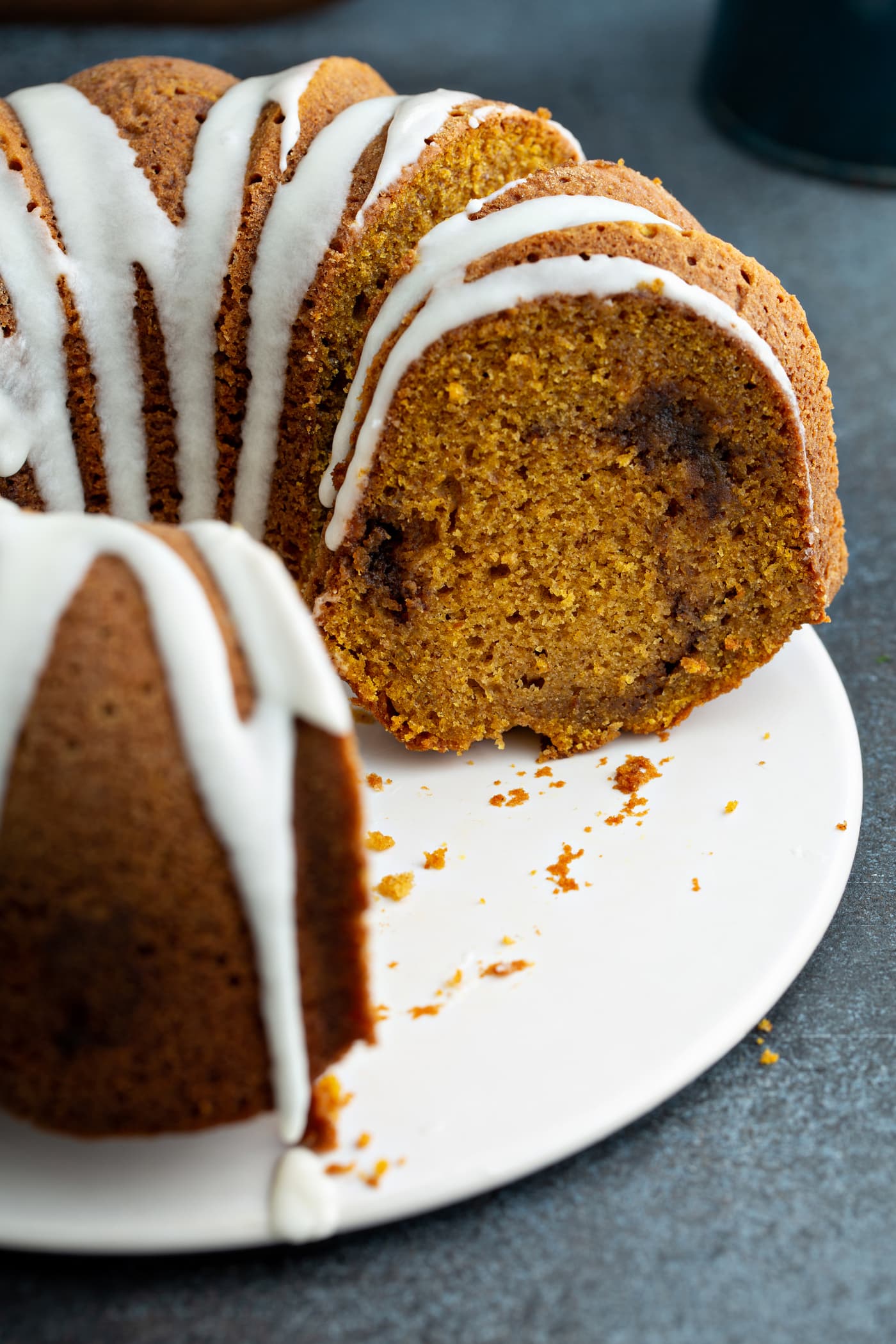 A sour cream cinnamon swirl pumpkin bundt cake with a few slices removed. The cake is drizzled with white glaze and you can see the cinnamon swirl in the middle of the cake.