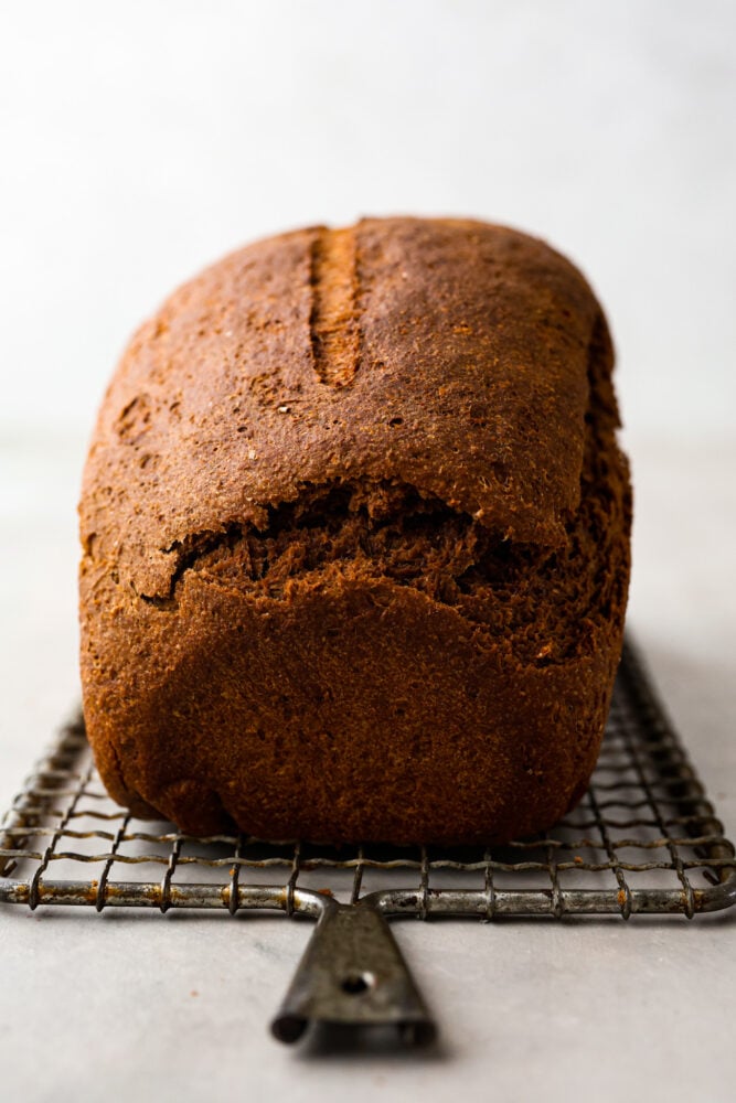 A side view of the loaf of pumpernickel bread on a wire rack.
