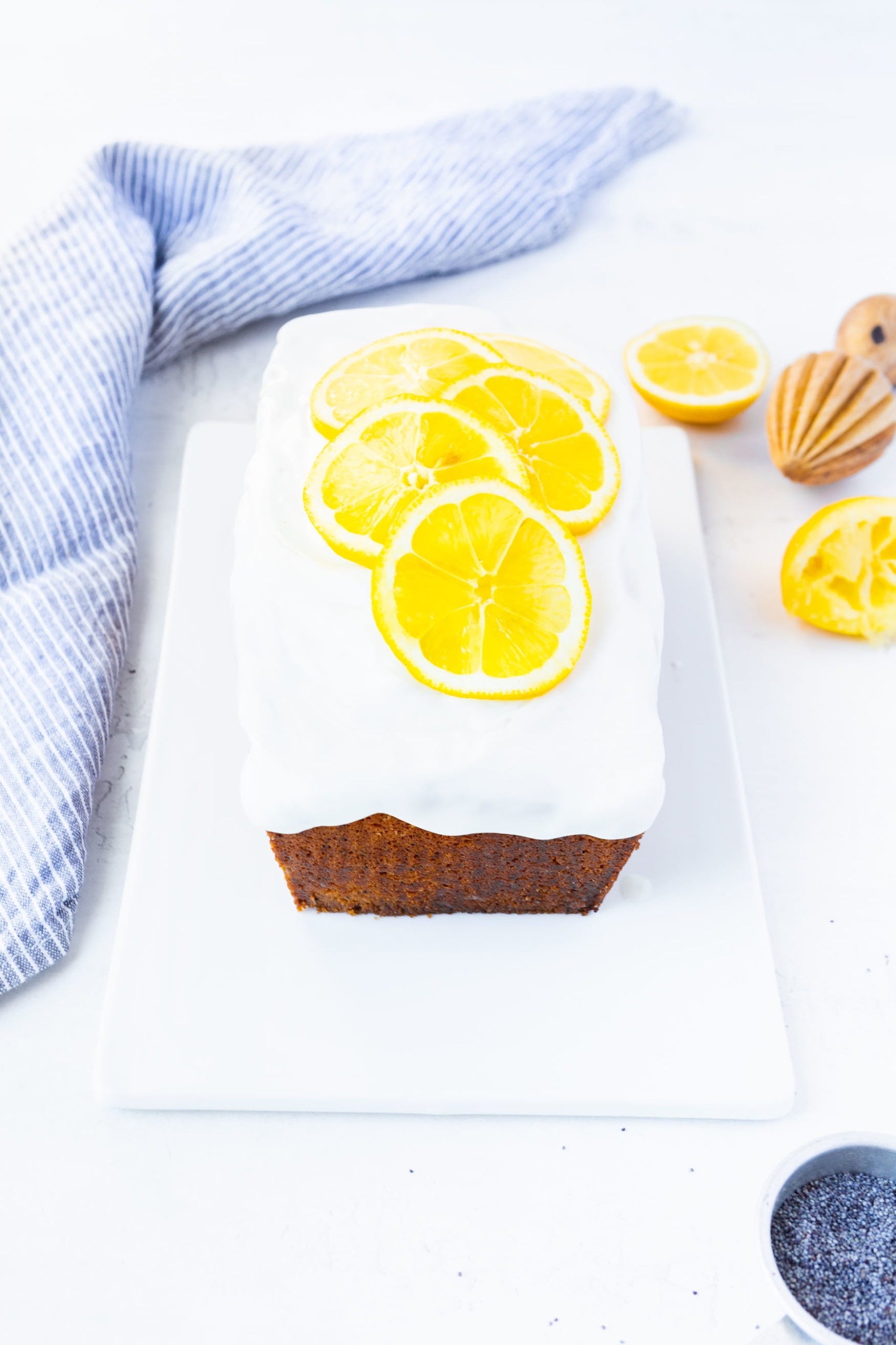 a photo of an iced lemon poppy seed loaf cake topped with bright white icing and thinly sliced lemon slices.