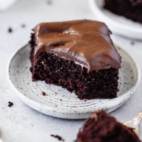 A piece of chocolate mayonnaise cake that has a bite taken out of it. It is frosted with chocolate cream cheese frosting. Other servings of cake are in the background.