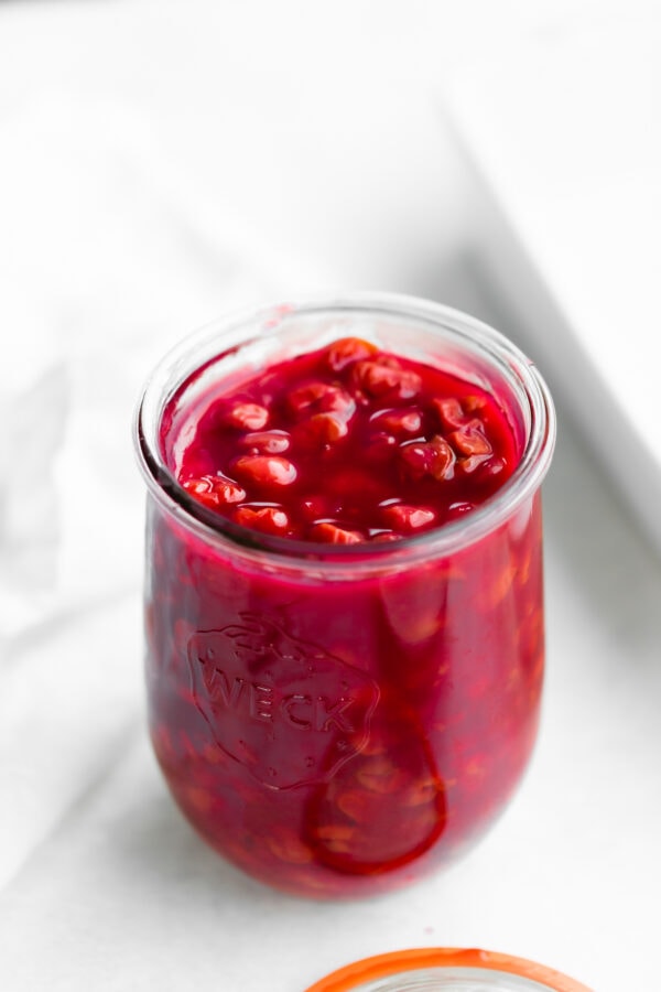 a photo of a glass jar of bright red cherry pie filling