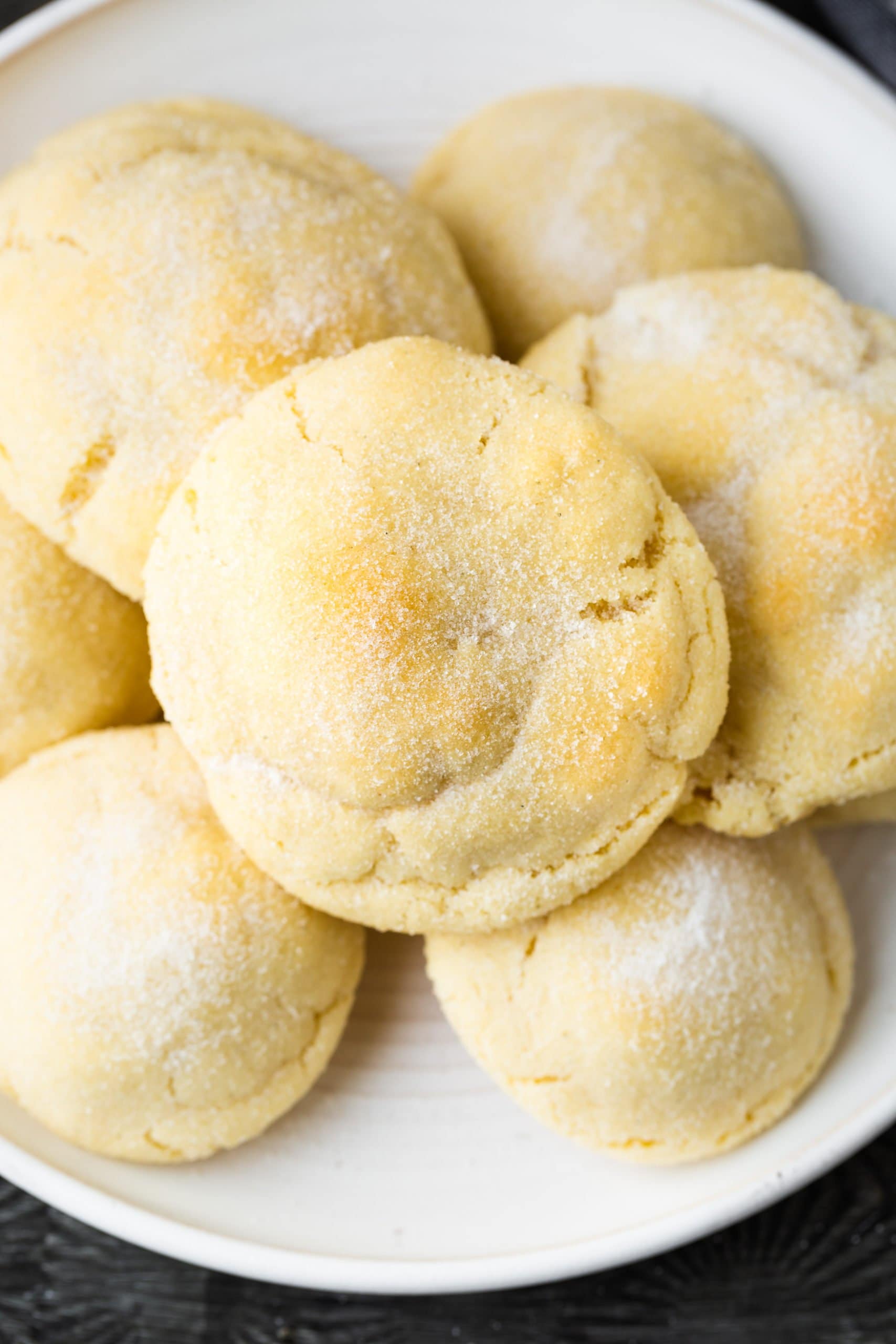 a photo of thick and slightly golden sugar cookies piled on a white plate.