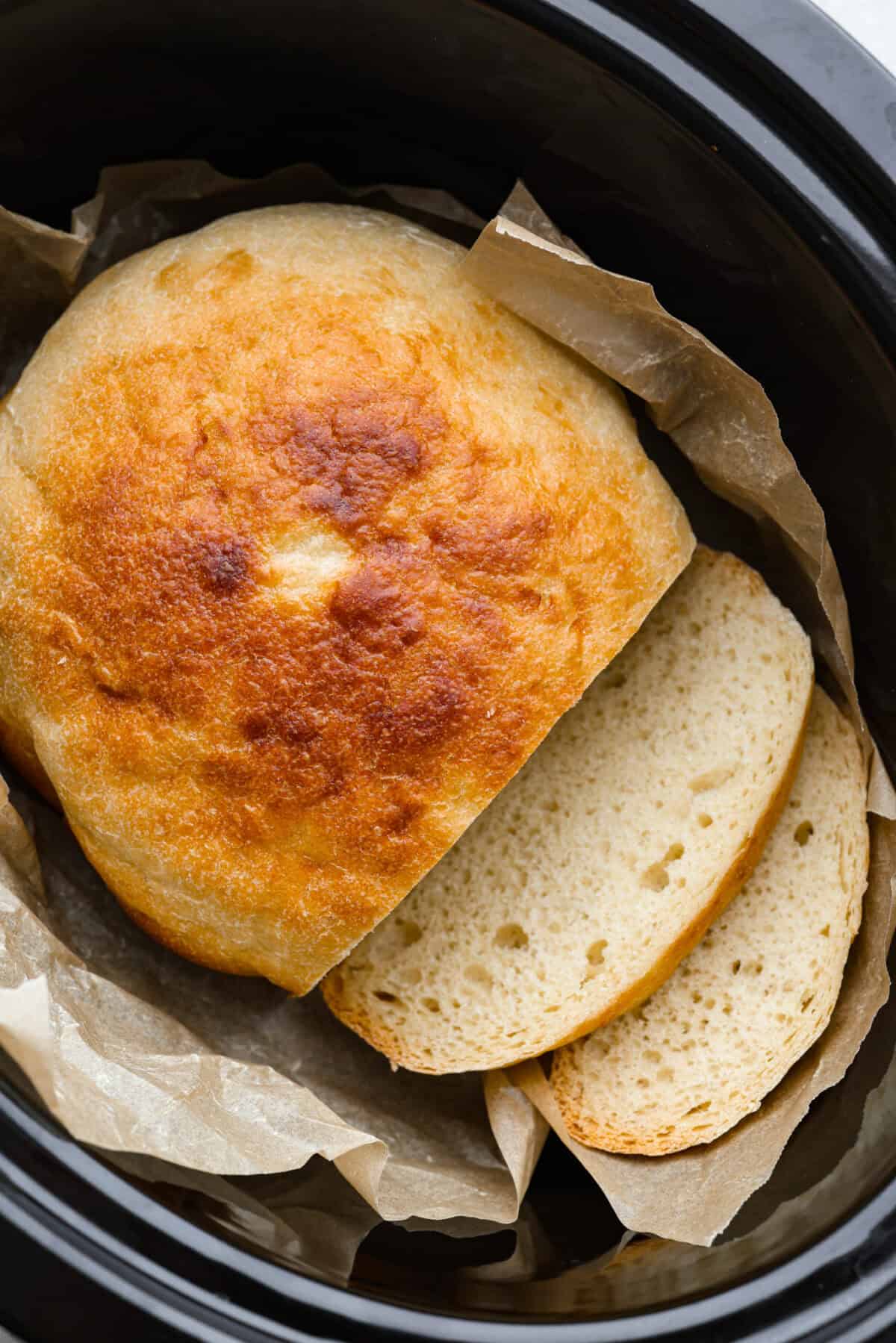Slow cooker bread inside of the slow cooker on the parchment paper. 