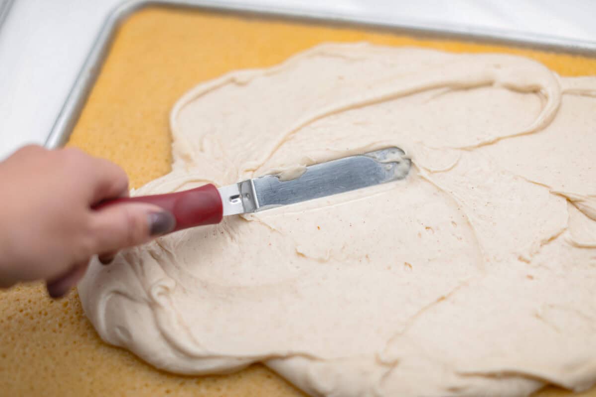 Angle shot of someone spreading the frosting over the cooled sheet cake. 
