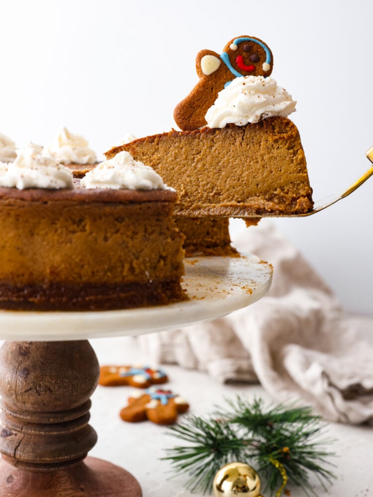 A gingerbread cheesecake on a stand with a scoop being taken out of it.
