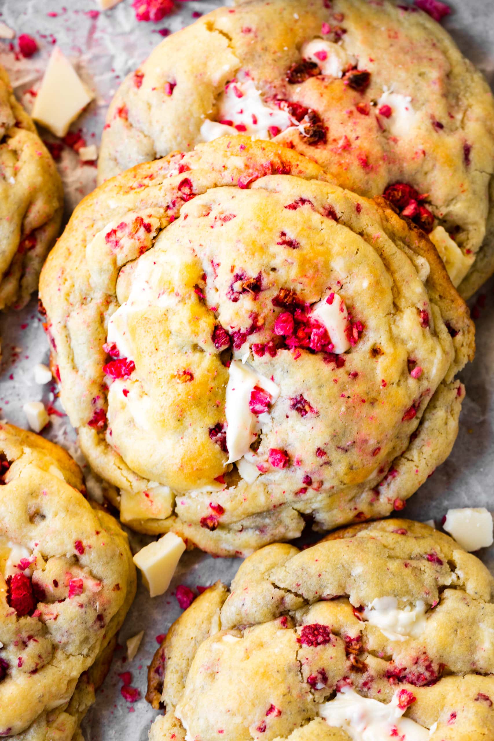 a photo of a large thick and golden white chocolate raspberry cookie sitting next to several other cookies.
