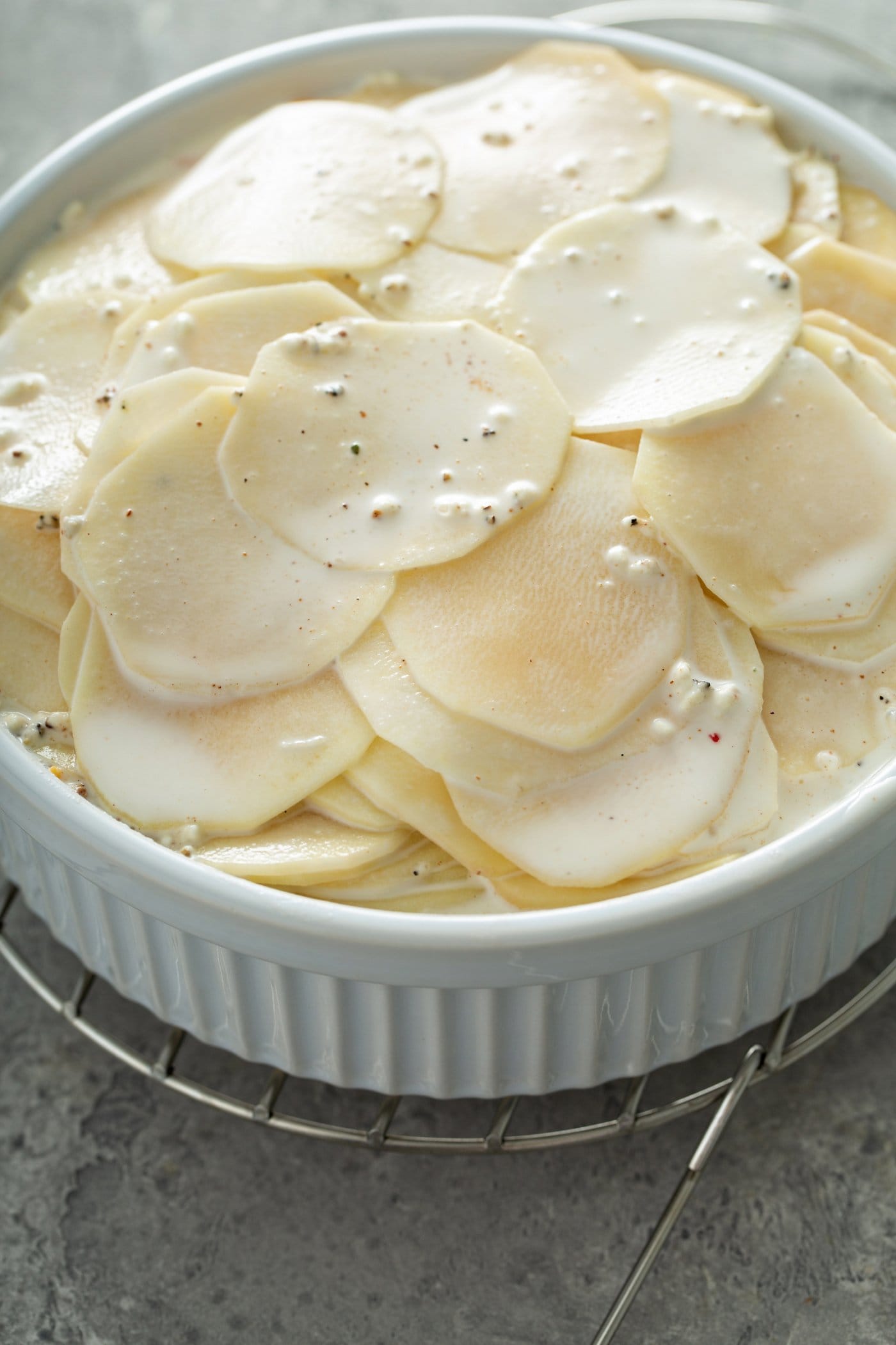 A casserole dish filled with sliced raw potatoes. A cream sauce is poured over the top.