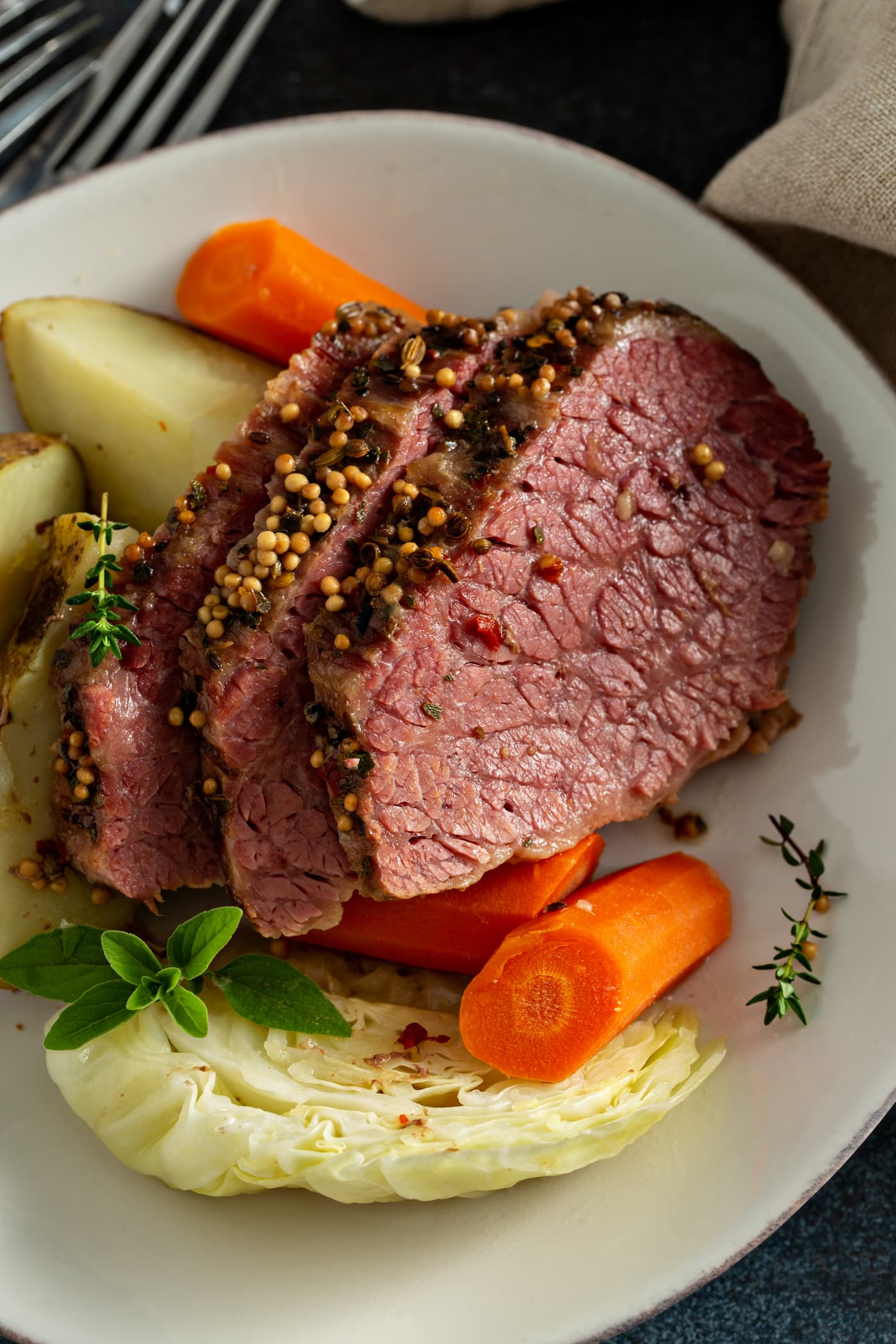Three slices of corned beef with carrots and potatoes and cabbage on a white plate.