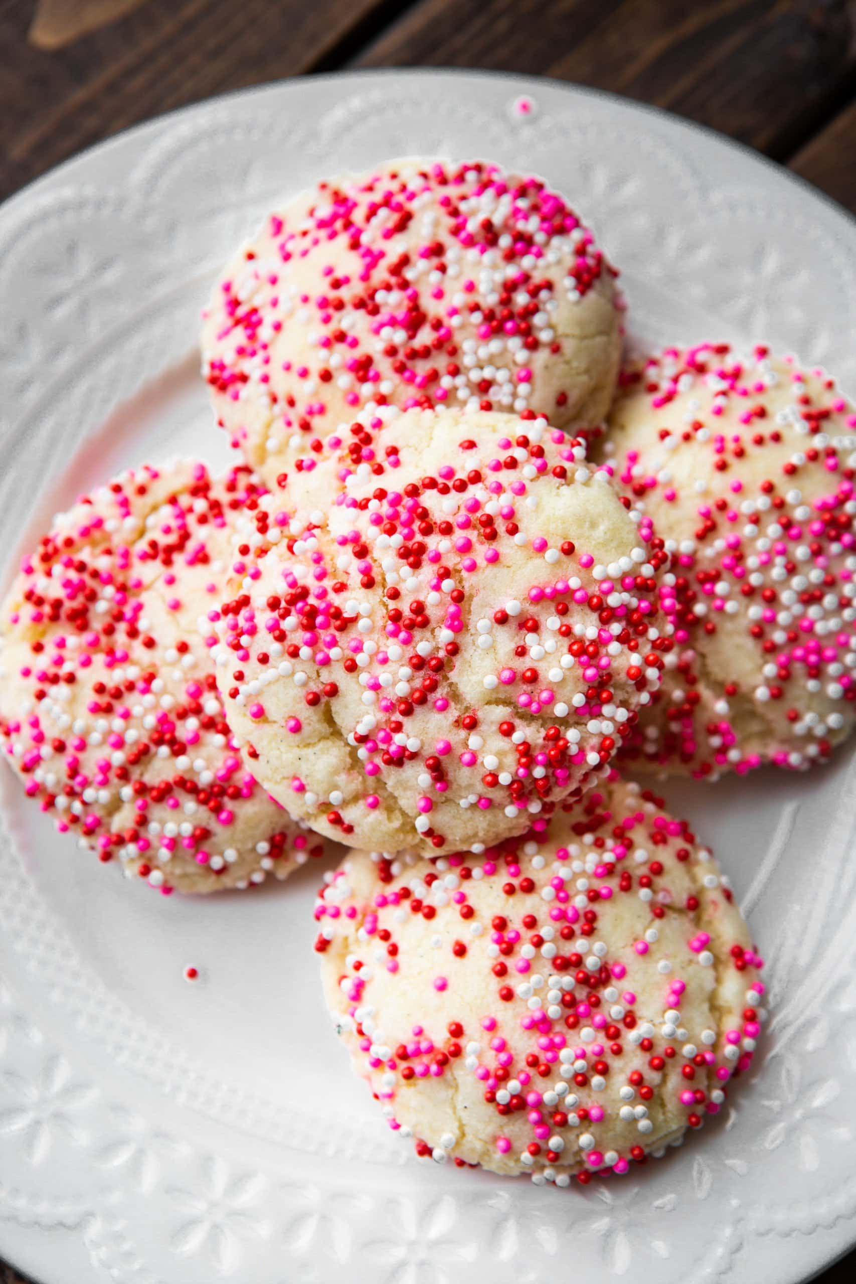 a photo of five sugar cookies with red, pink and white sprinkles on them. the cookies are thick and pillowy.