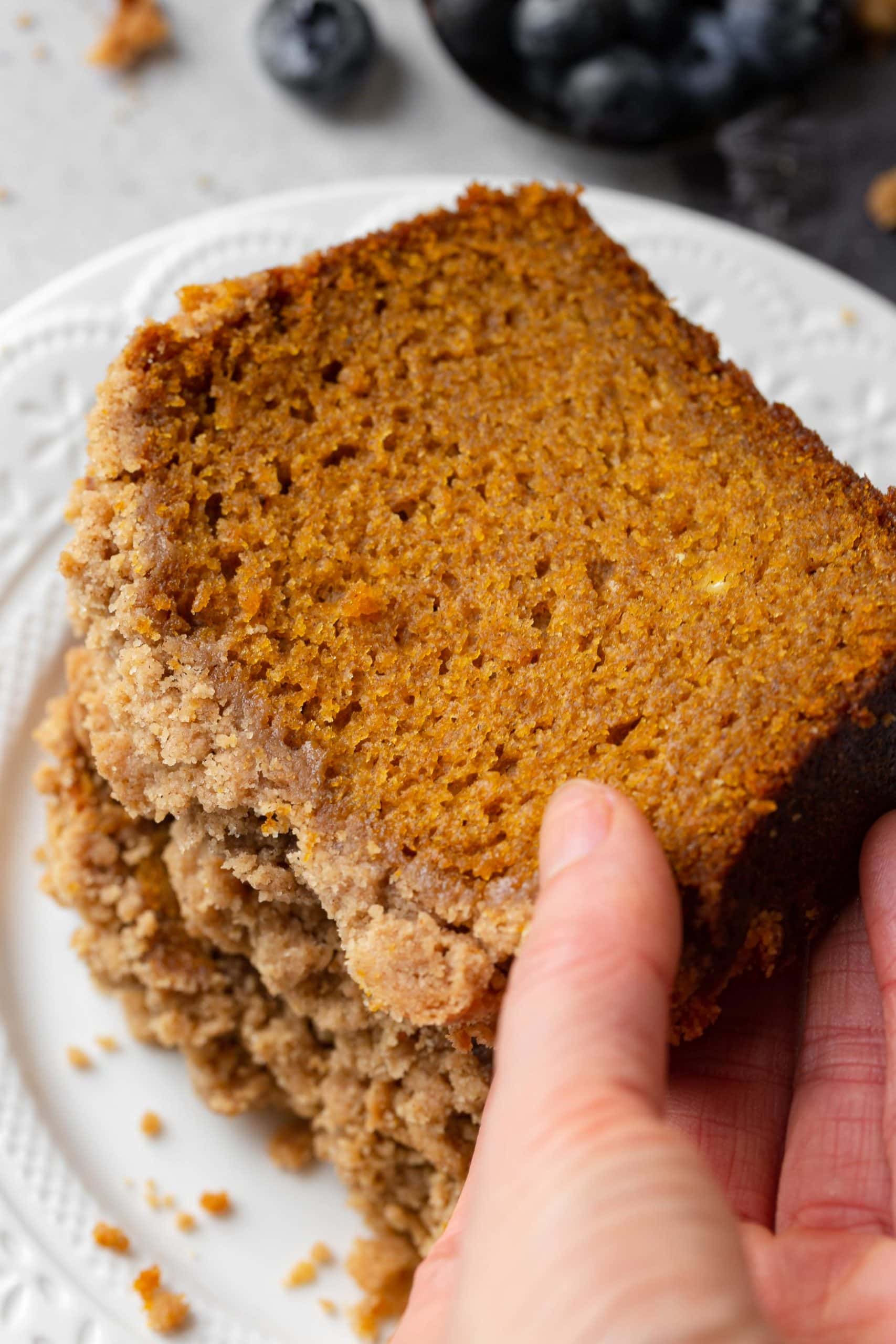 a photo of someone grabbing the top slice of pumpkin bread with streusel topping from a stack of slices.
