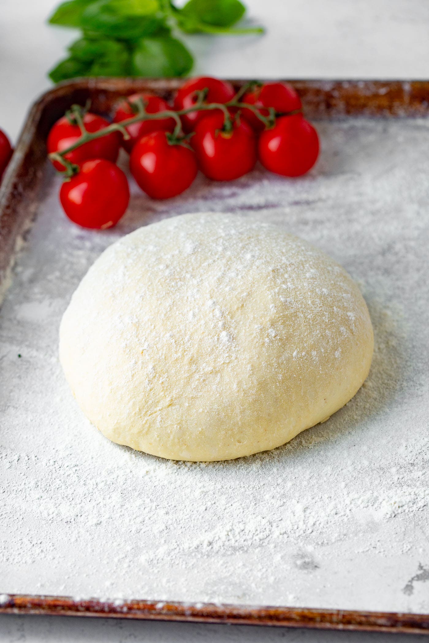 A ball of pizza dough with cherry tomatoes in the background.