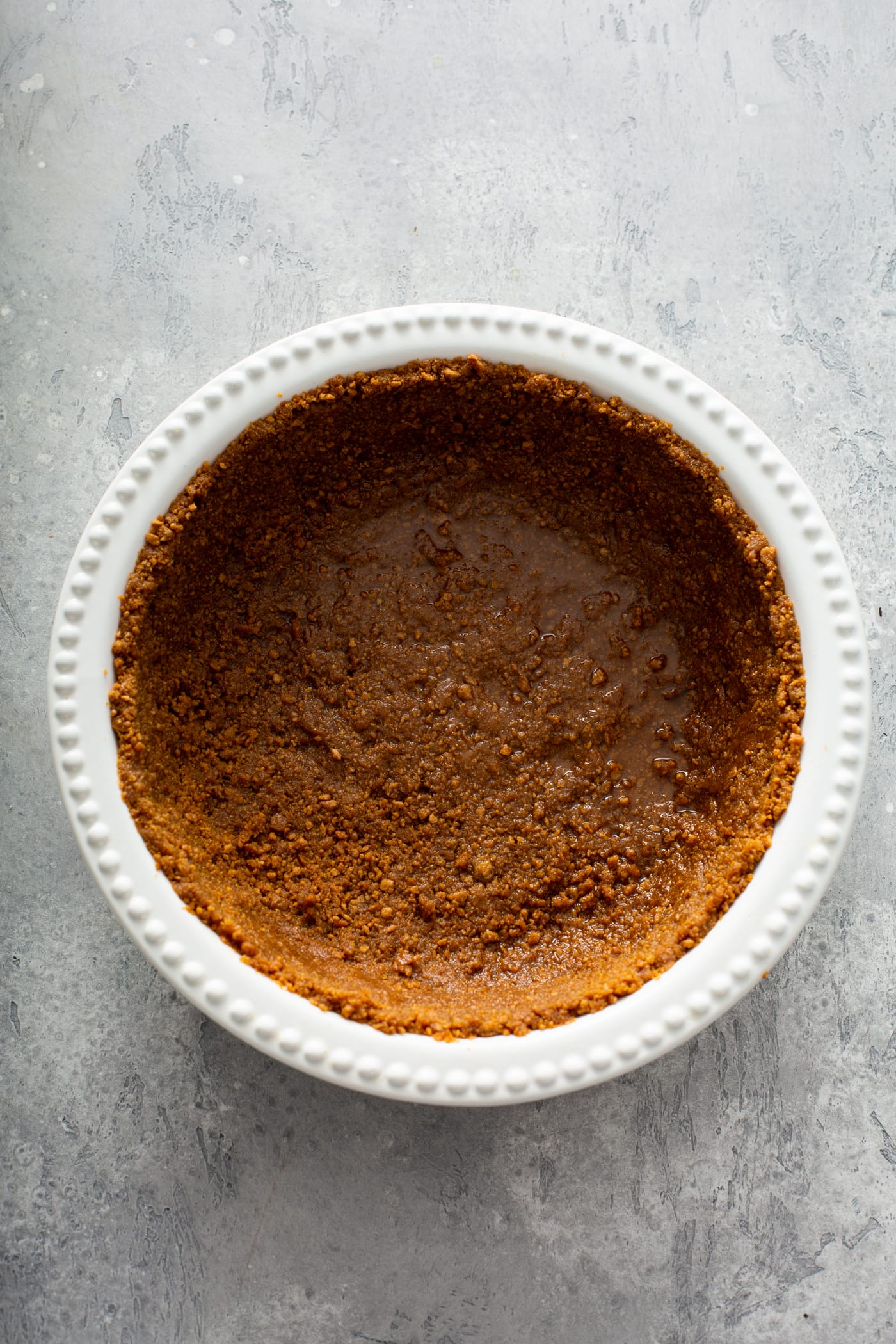 A white pie dish with a gingersnap crust in it.