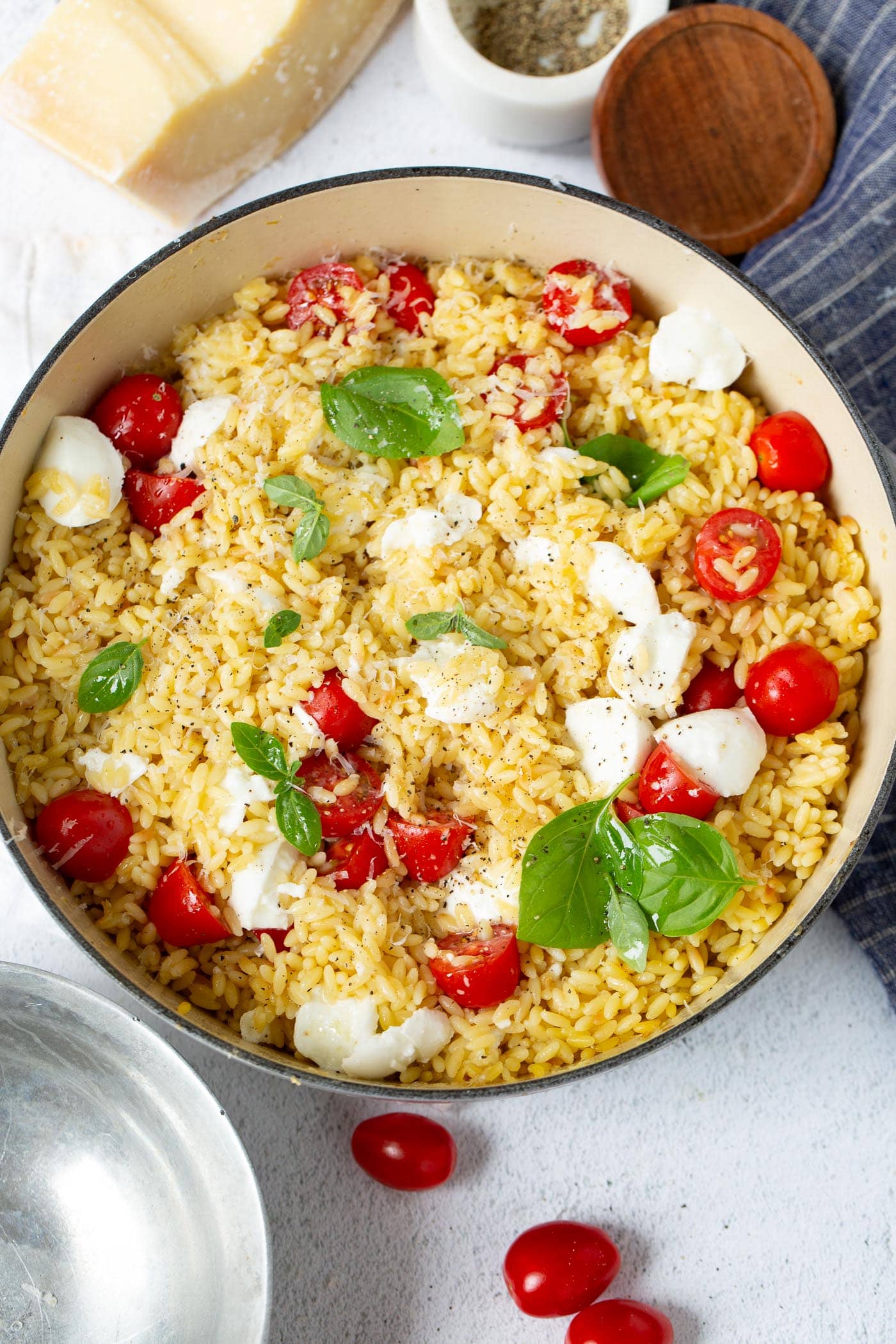 A bowl of caprese orzo salad. There are tomatoes and mozzarella chunks and fresh green basil in the salad.