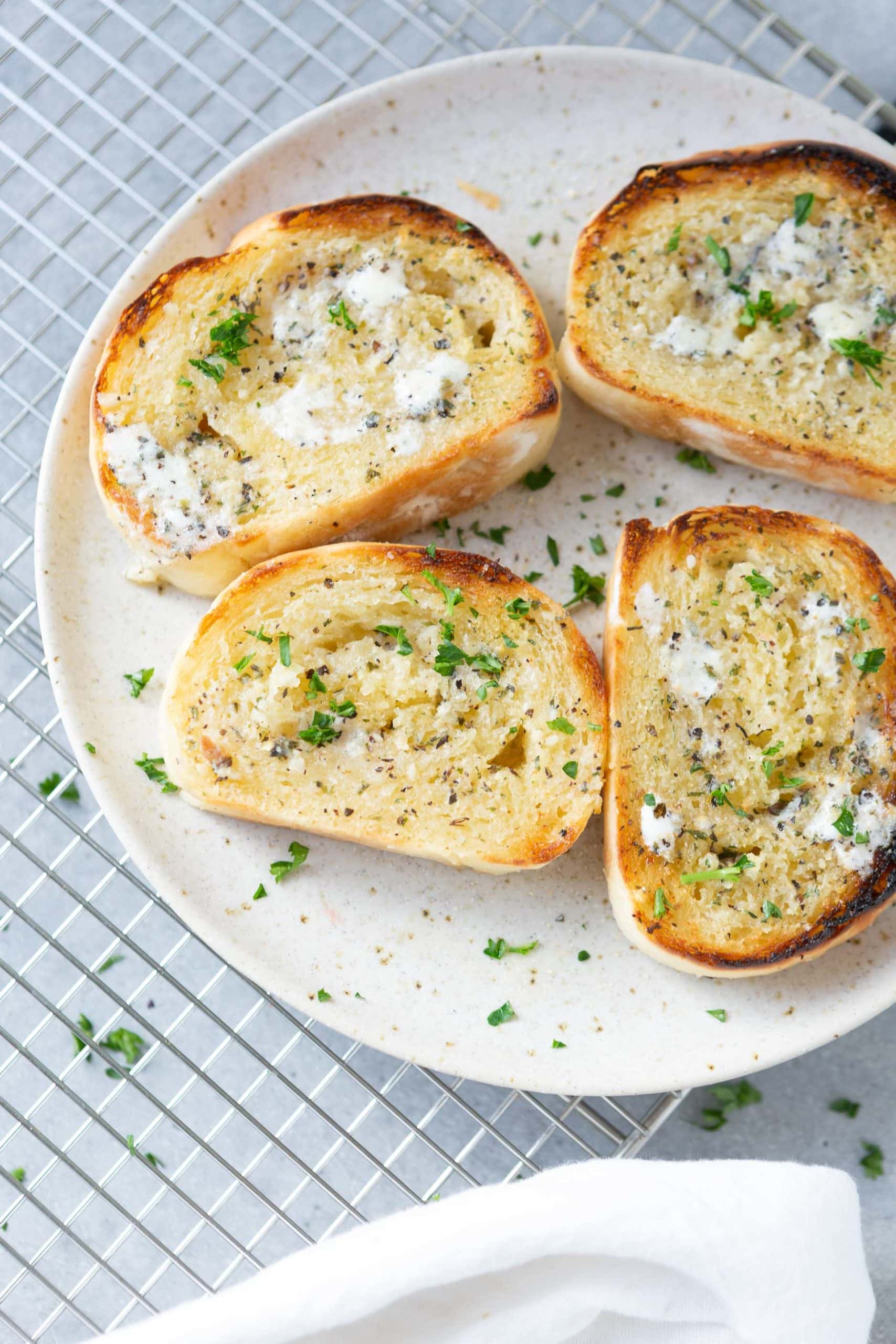 a photo of several slices of buttery toasted garlic bread sprinkled with chopped parsely sitting on a white plate