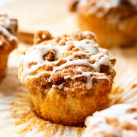 an apple coffee cake muffin sitting on an open paper liner with streusel and icing