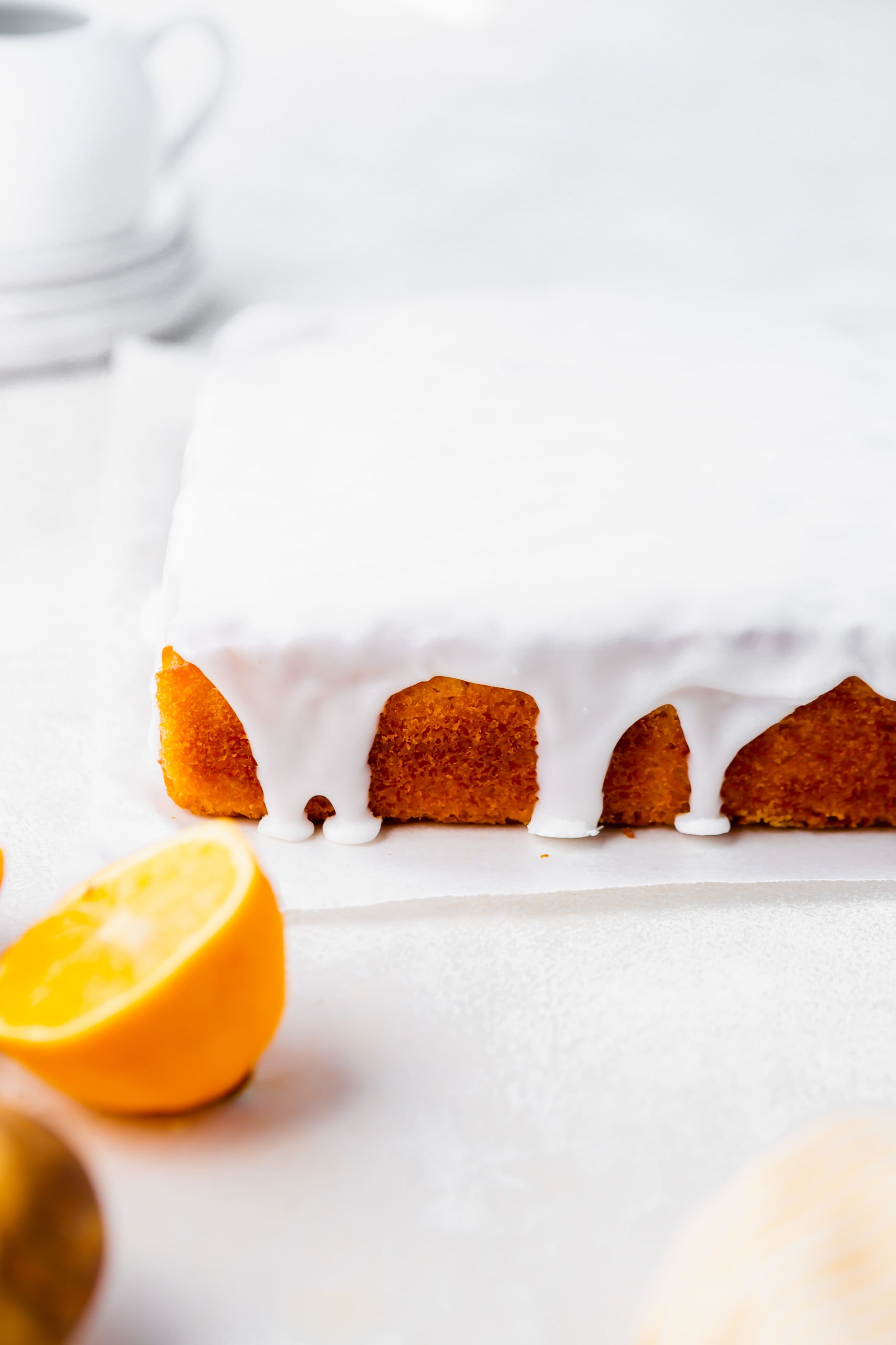 a photo of a square lemon cake that has been covered in a white lemon glaze that is dripping down the sides.
