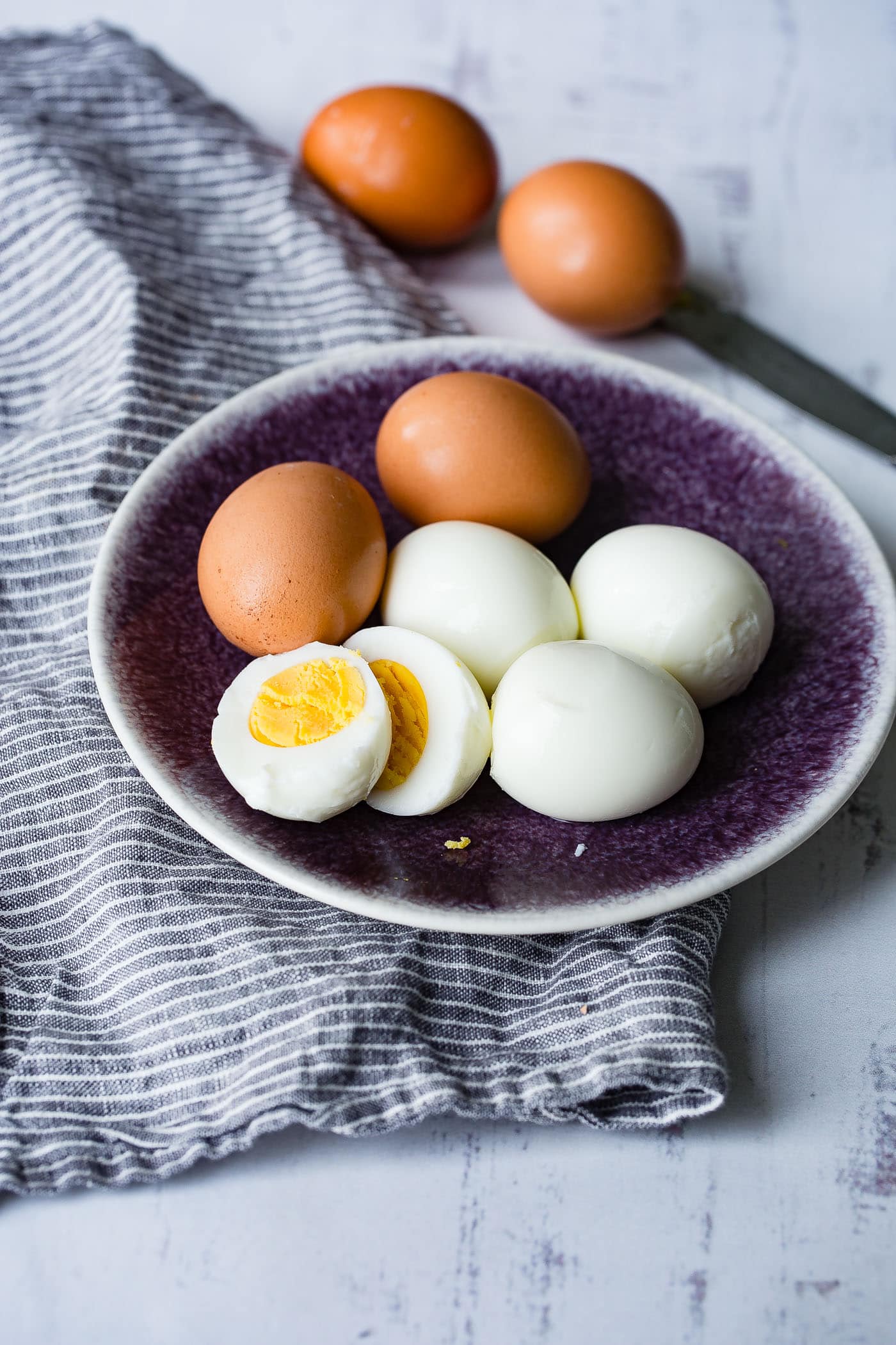 A plate with 6 hard boiled eggs. There are two brown eggs, three that have been peeled and one that is peeled and cut in half with a perfectly cooked yolk.