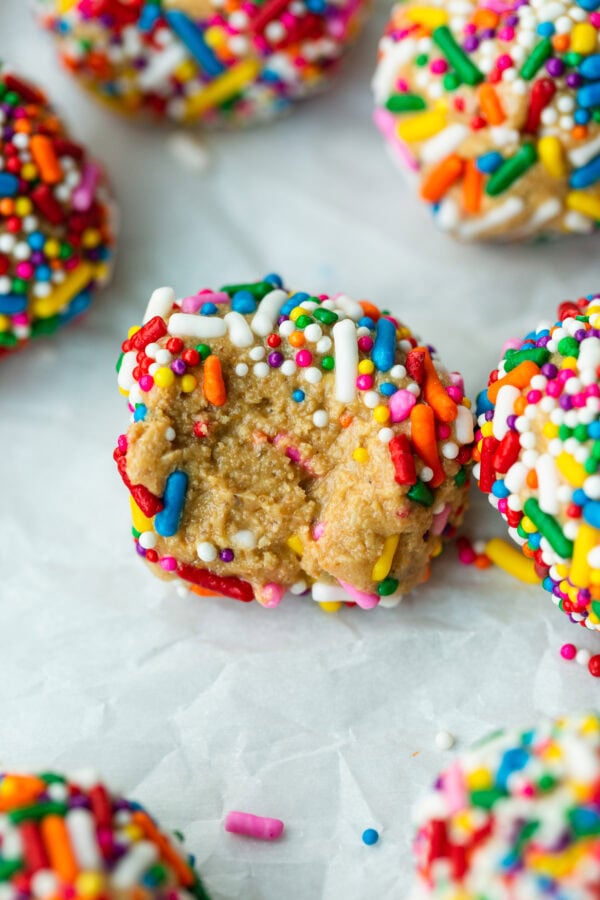 a photo of several protein bites covered in rainbow sprinkles with one that has a bite taken out of it