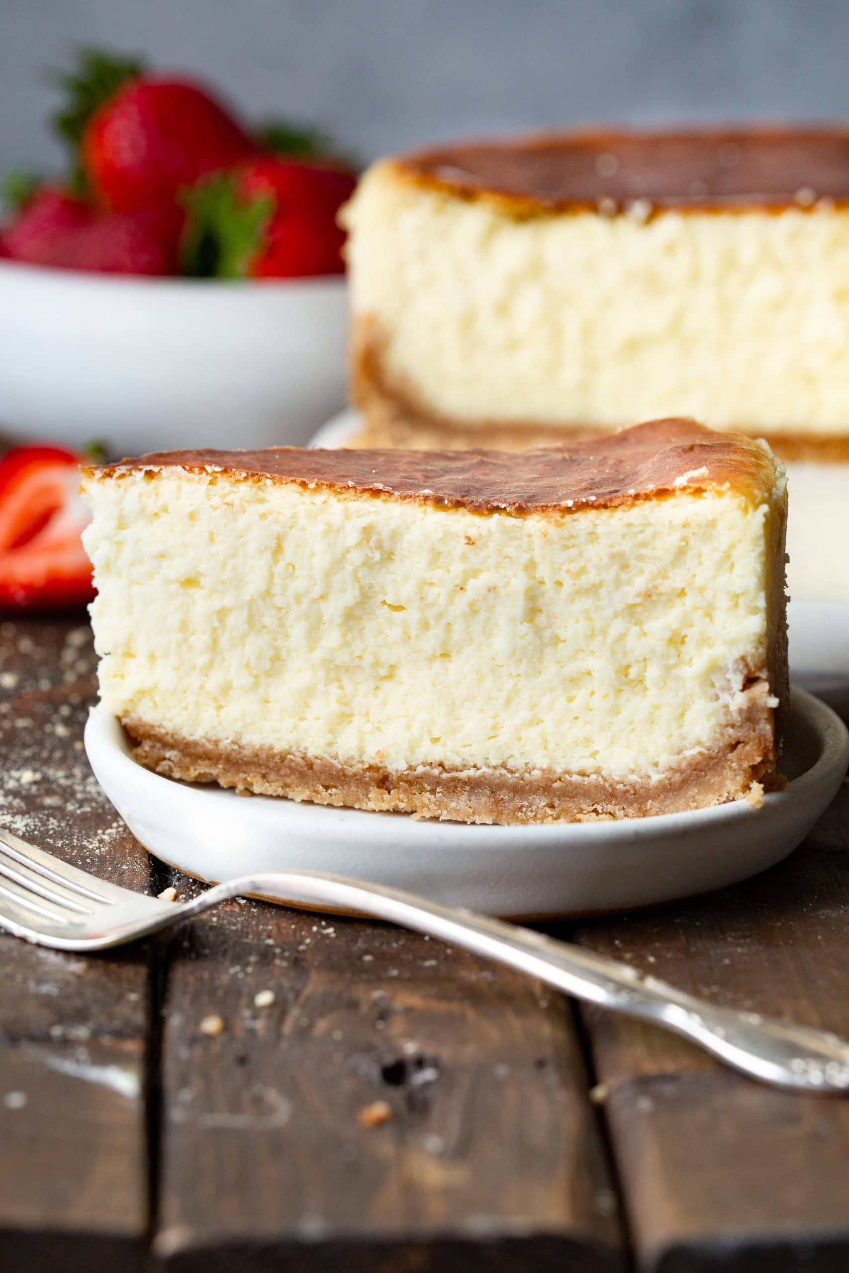 a photo of a large slice of classic cheesecake taken from the side so you can see the cross-section. It has a thick graham cracker crust and golden top.