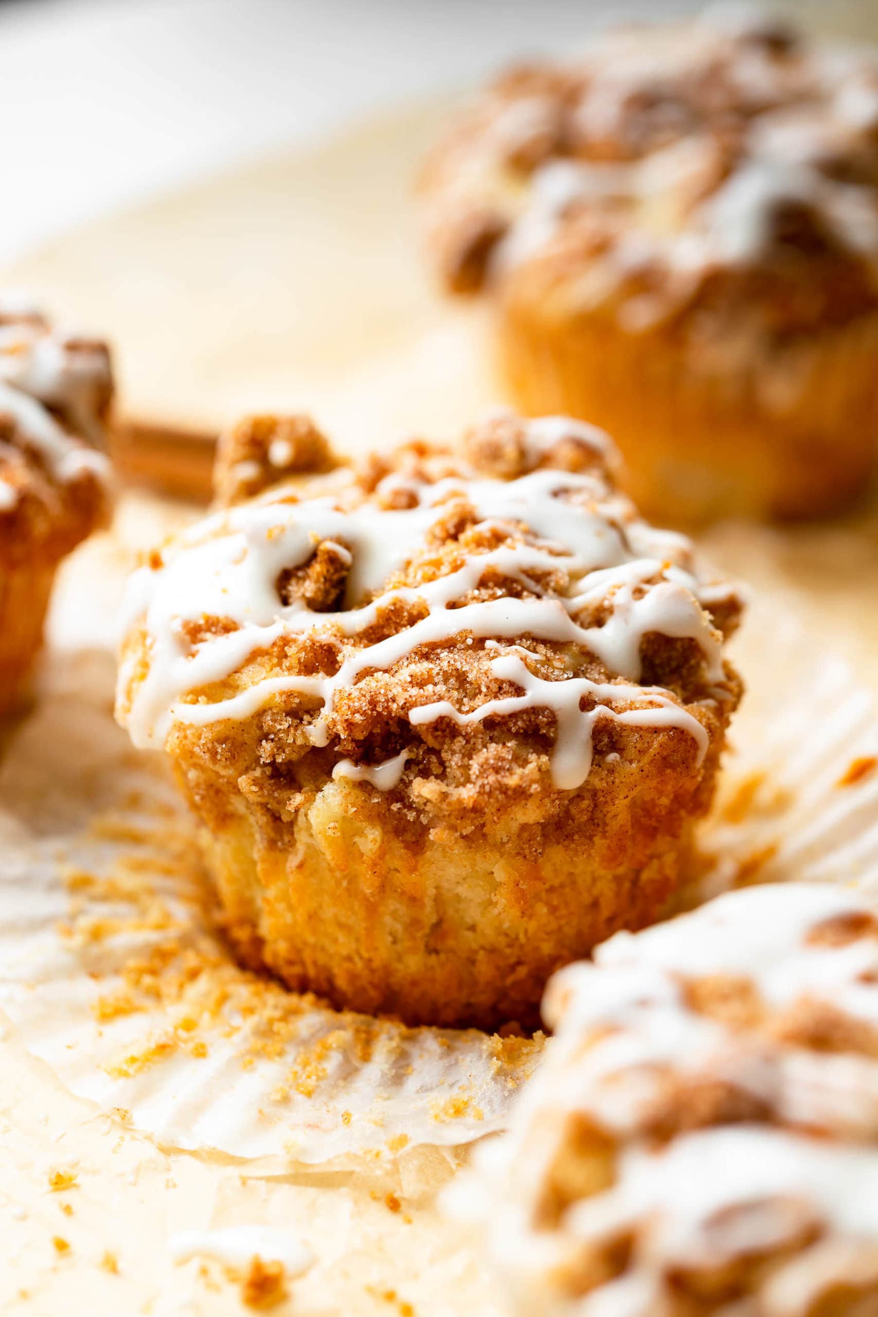 an apple coffee cake muffin sitting on an open paper liner with streusel and icing