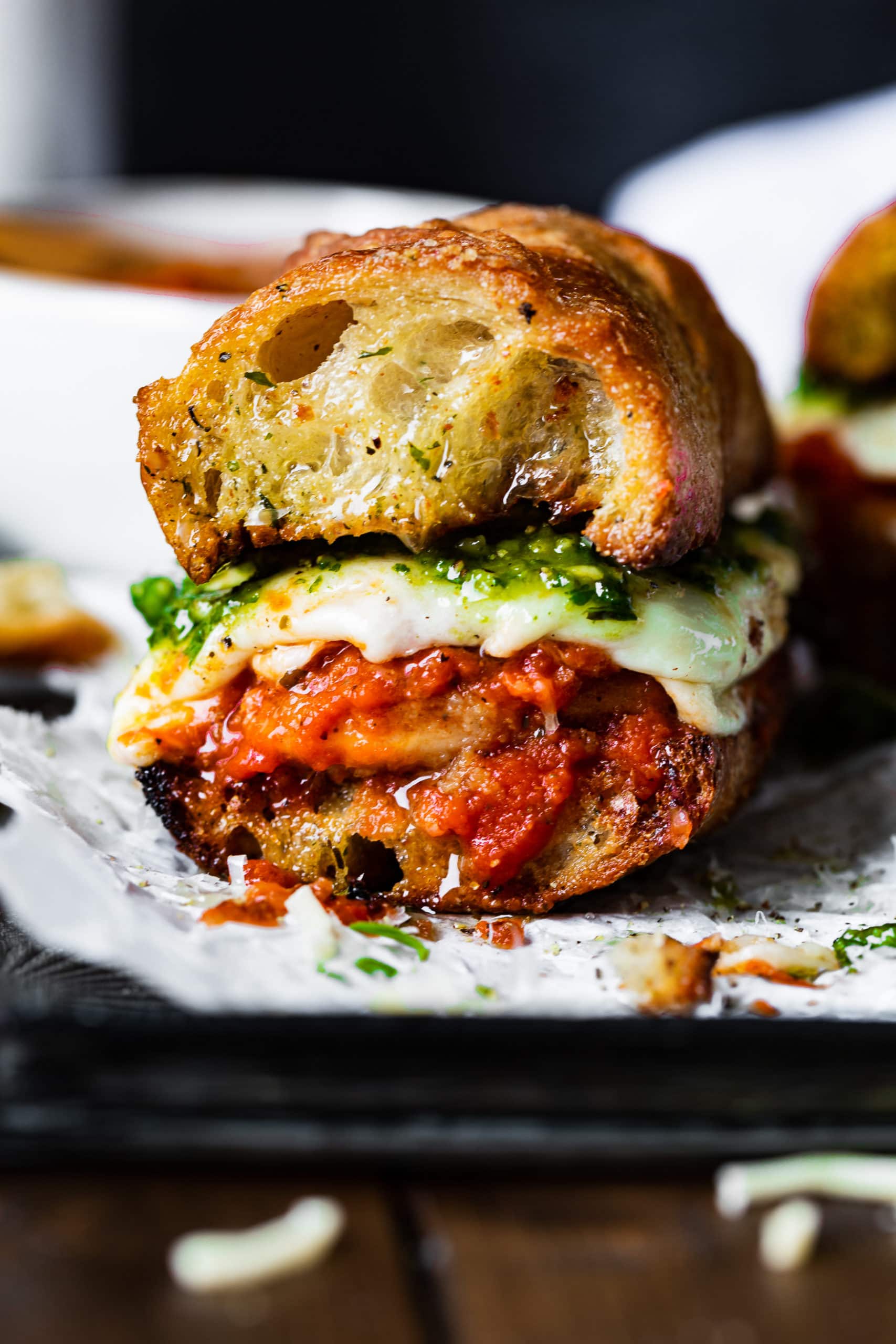 a photo of the cross section of a chicken parmesan sandwich with gooey cheese, marinara sauce, and pesto all sandwiched in buttery garlic bread.