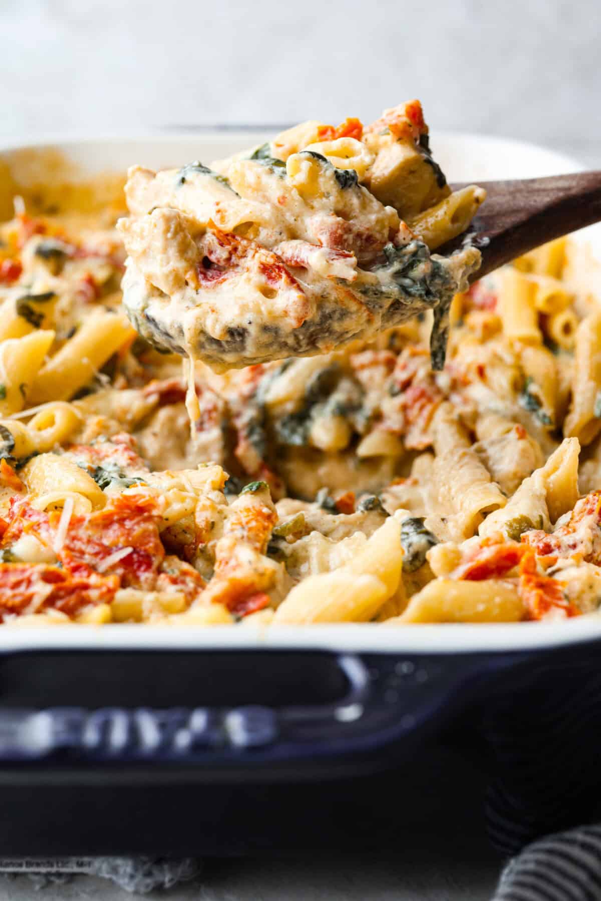 Shot of some one lifting a portion of tuscan chicken casserole out of the baking dish. 