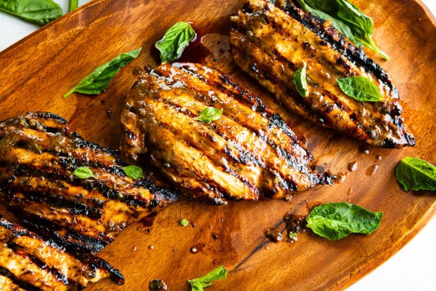 several grilled chicken breasts with basil leaves scattered about it