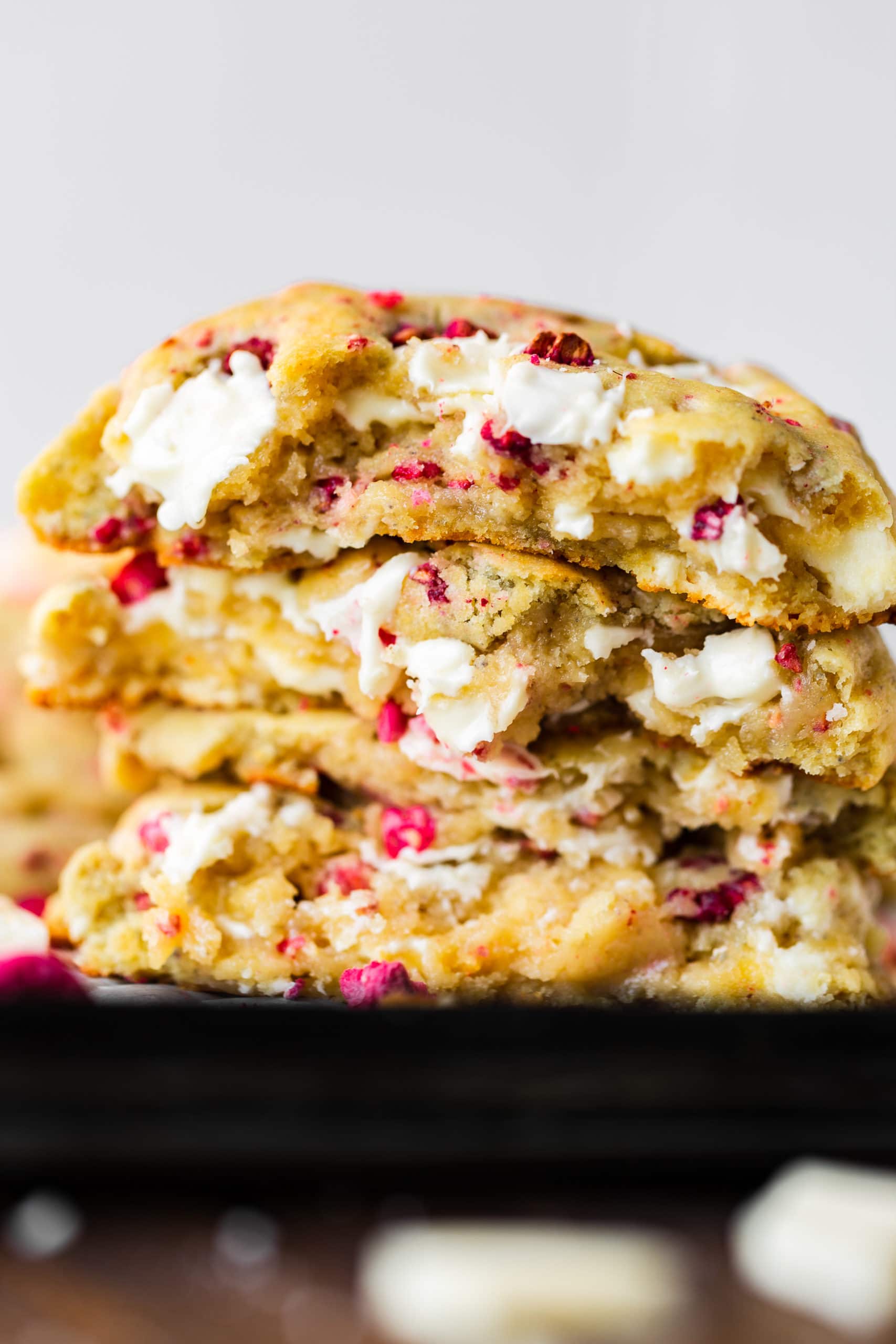 a photo of three golden white chocolate chip raspberry cookies that have been broken in half and then stacked on top of each other so you can see the chewy inside of the cookies.